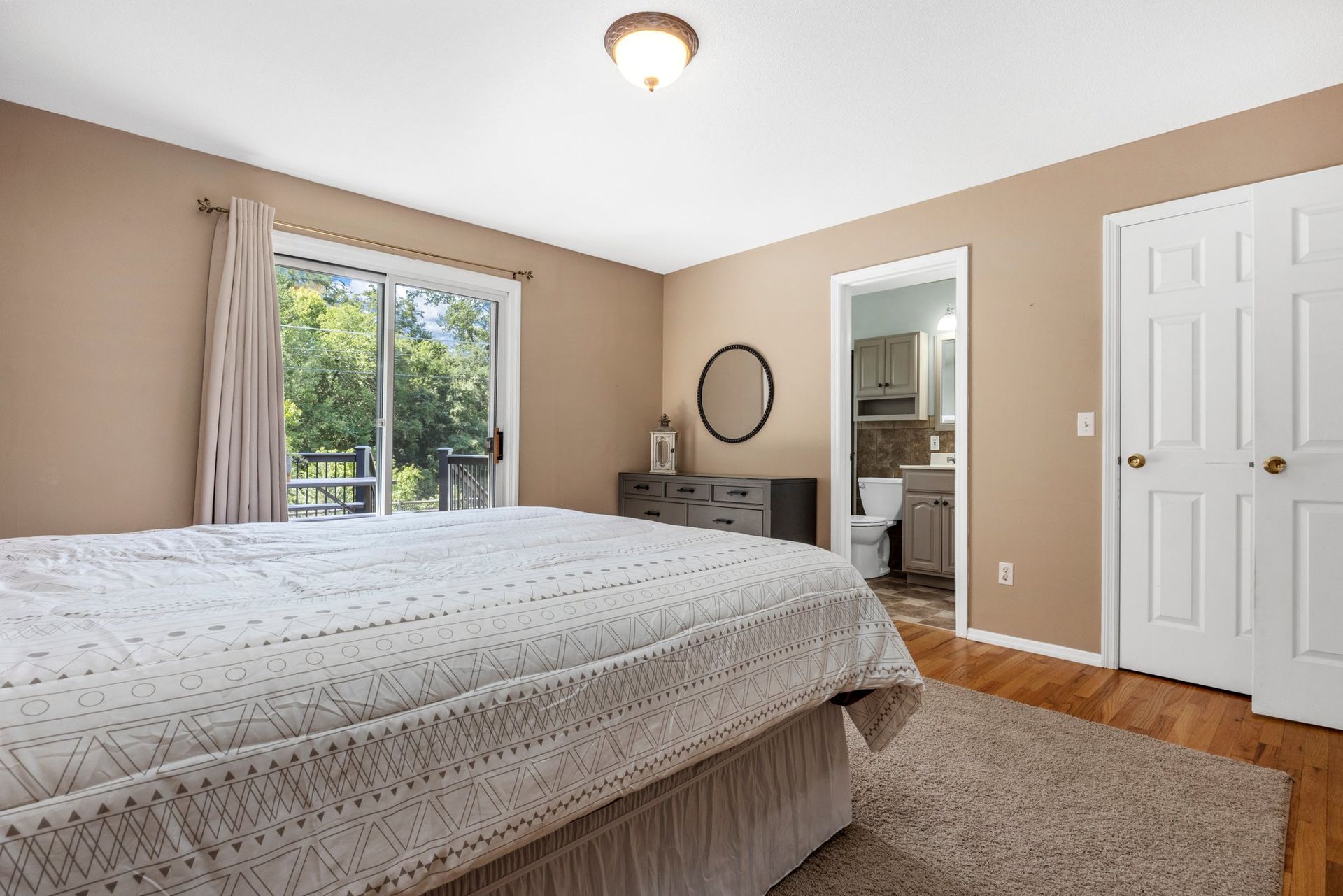 A bedroom with a bed , dresser , and sliding glass doors leading to a bathroom.