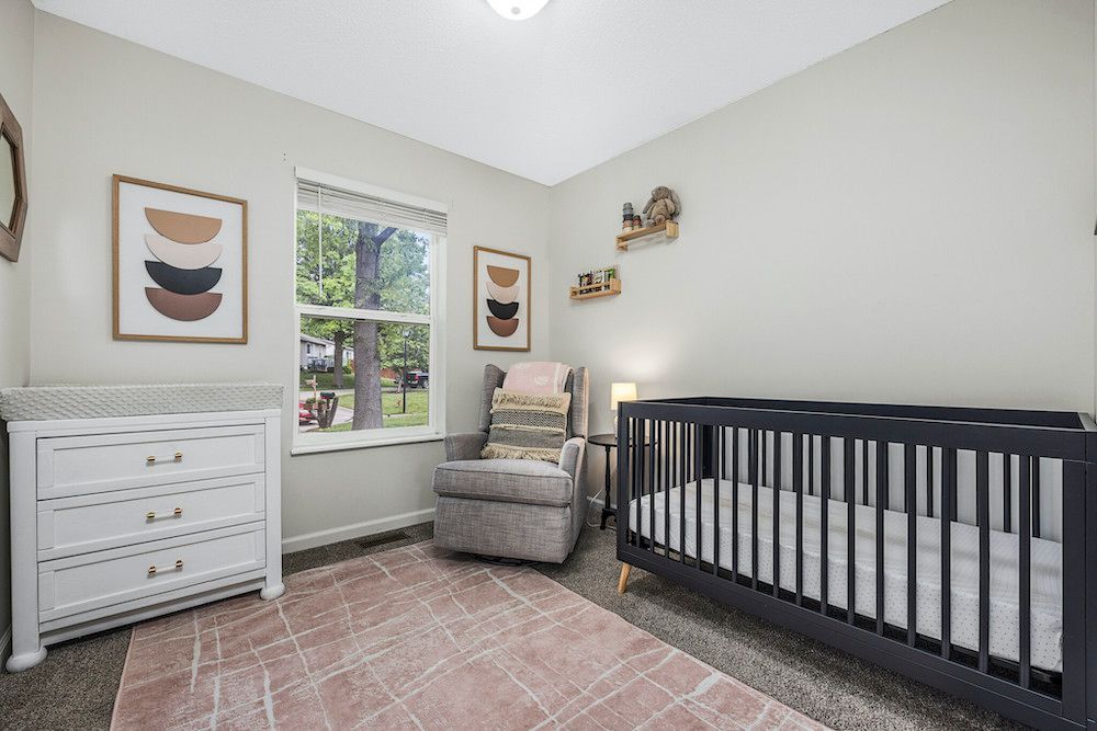 A nursery with a crib , chair , dresser and window.