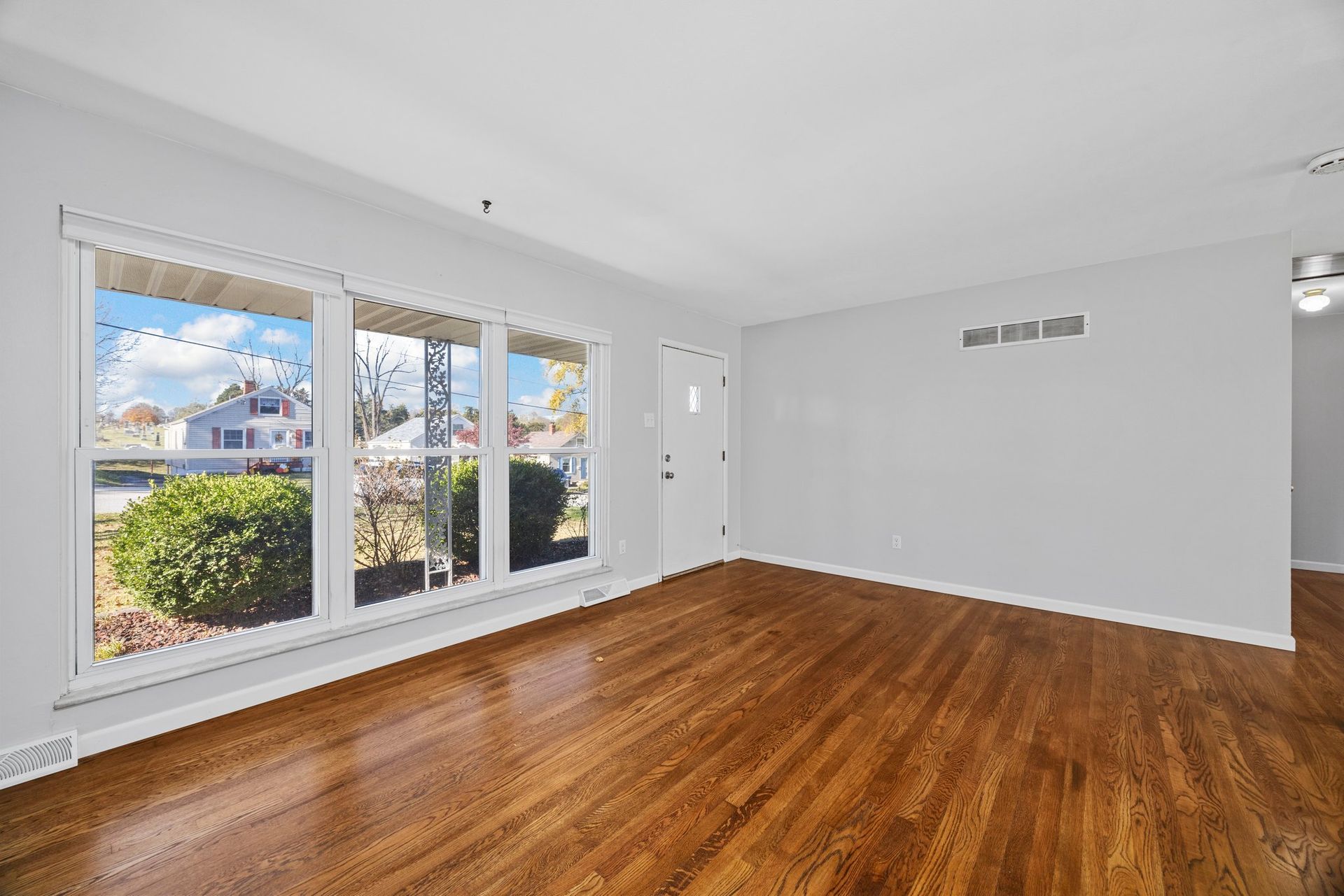 An empty living room with hardwood floors and lots of windows.