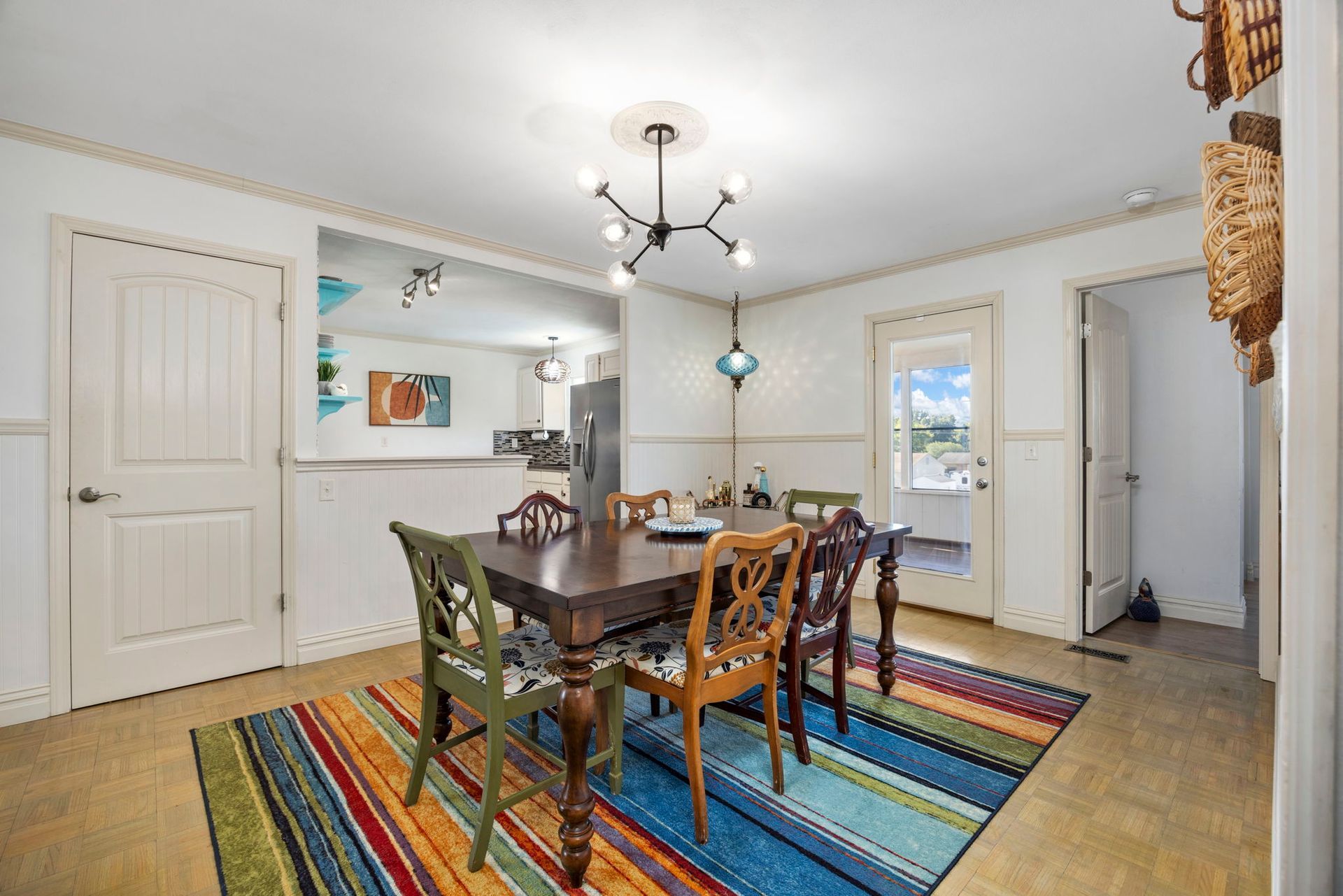 Dining room with a table, six mismatched chairs, and a colorful rug.