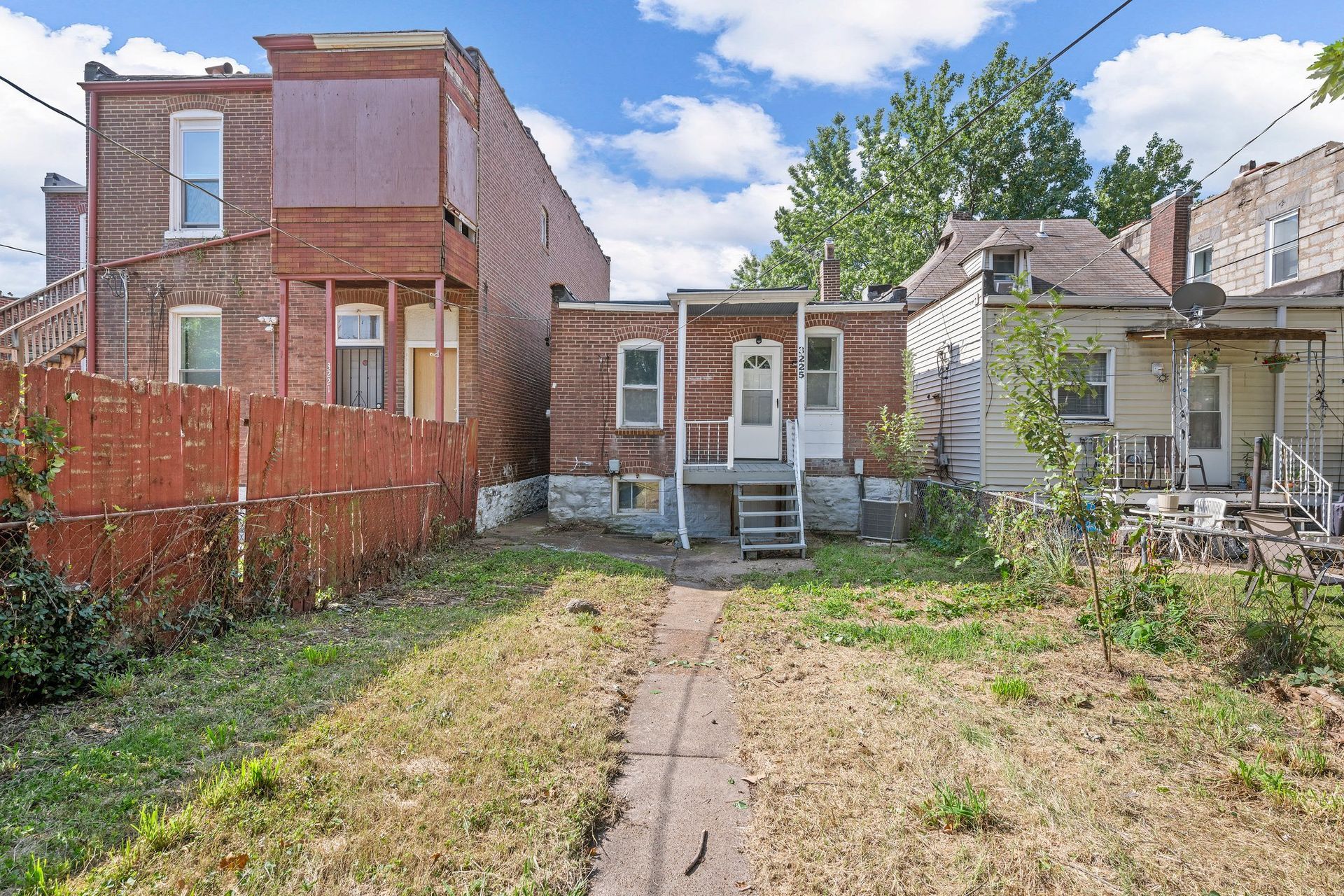 A backyard with a brick house and a white house in the background.