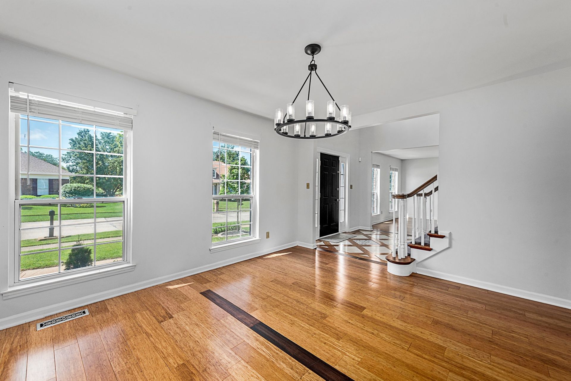 An empty living room with hardwood floors and a chandelier.