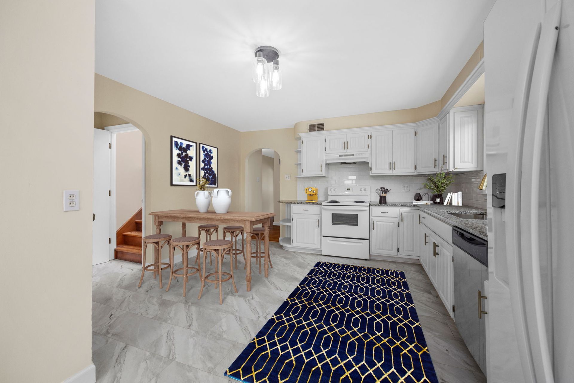 A kitchen with white cabinets , a refrigerator , a table and chairs , and a blue rug.