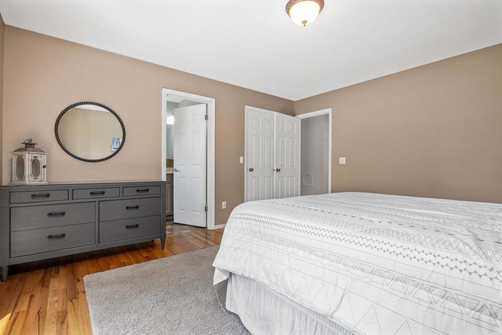 A bedroom with a bed , dresser , mirror and hardwood floors.