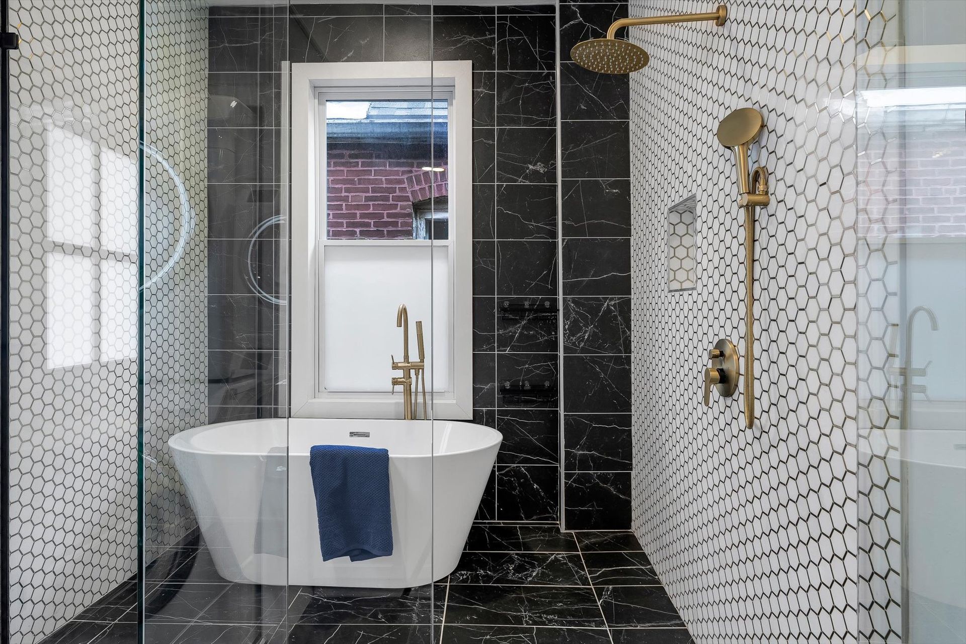 Modern bathroom with a freestanding tub, black and white tile, and gold fixtures.