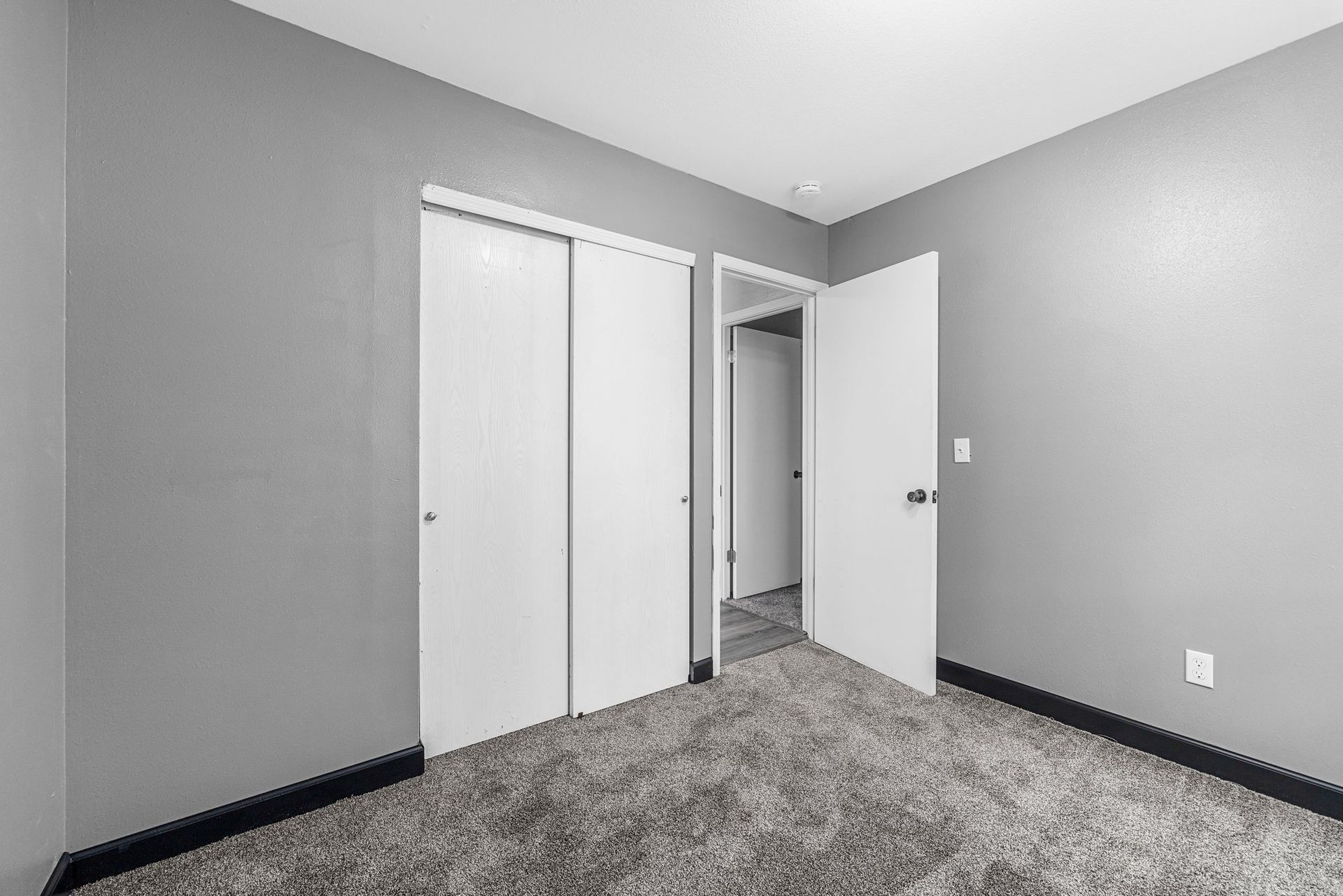An empty bedroom with a gray carpet and white doors.