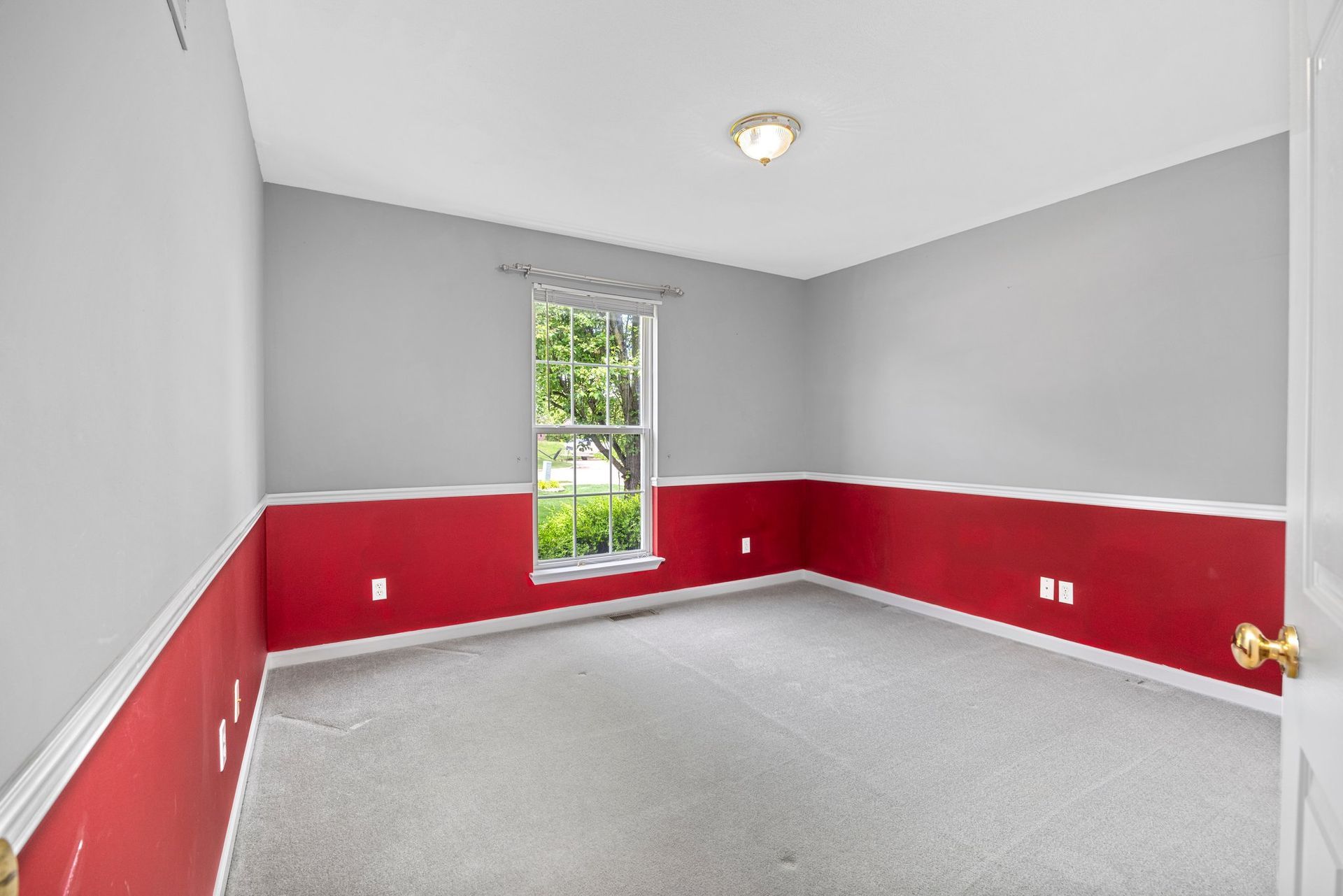 An empty room with red and gray walls and a window.