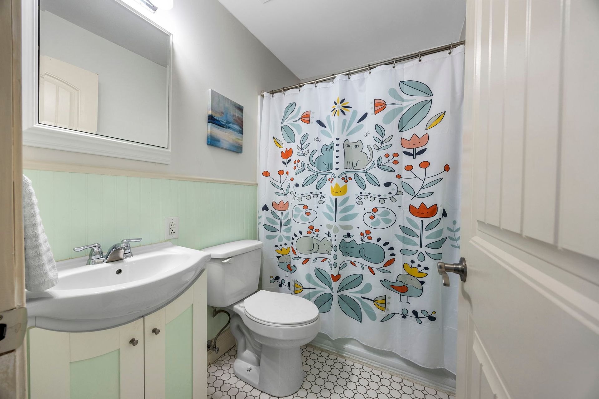 Bathroom with floral shower curtain, white sink, and toilet; mint green backsplash and walls.