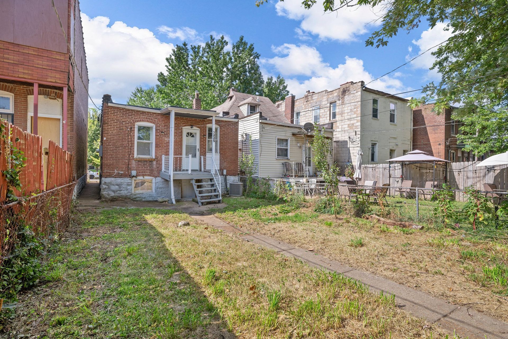 A backyard with a brick house and a white house in the background.
