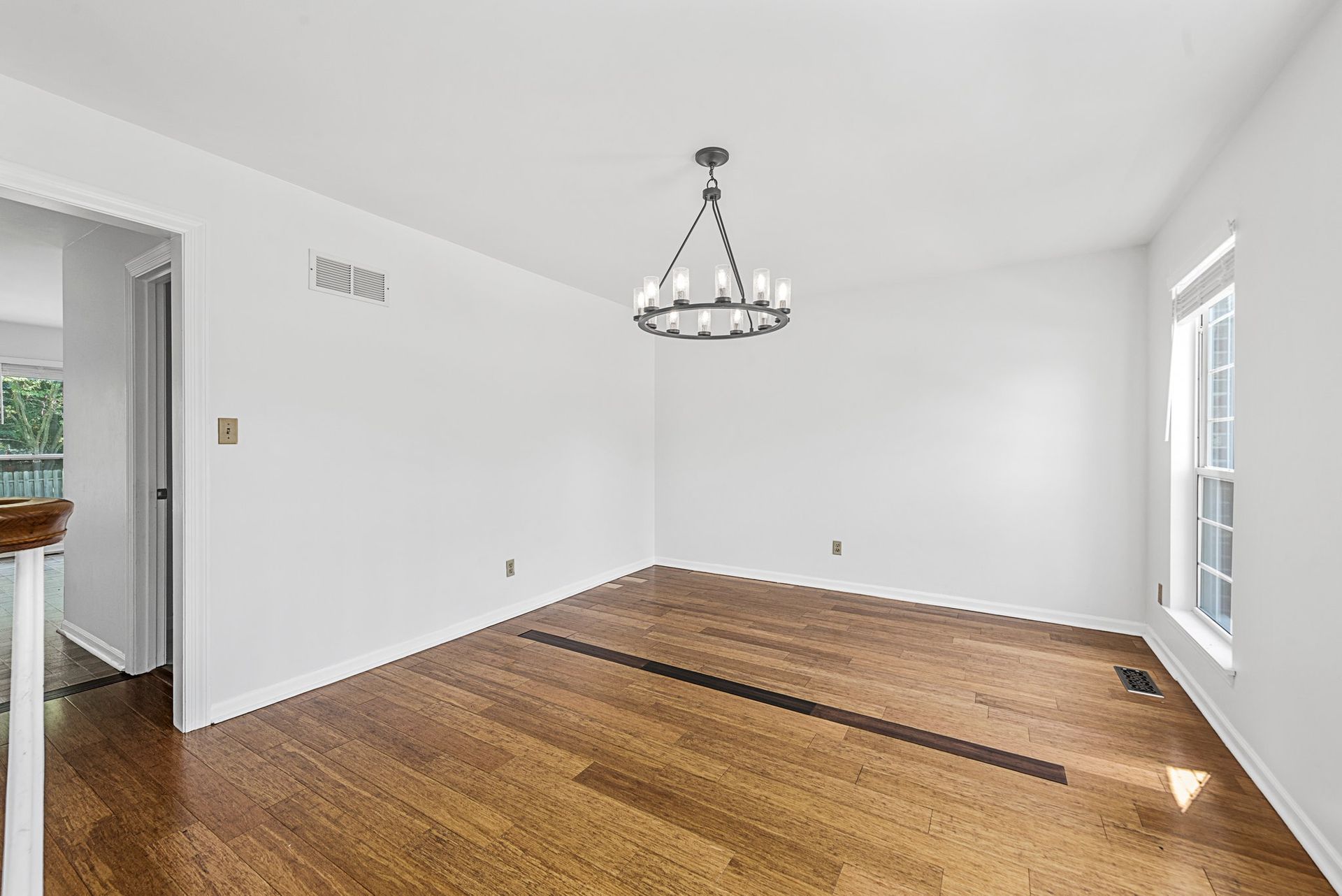 An empty living room with hardwood floors and a chandelier hanging from the ceiling.
