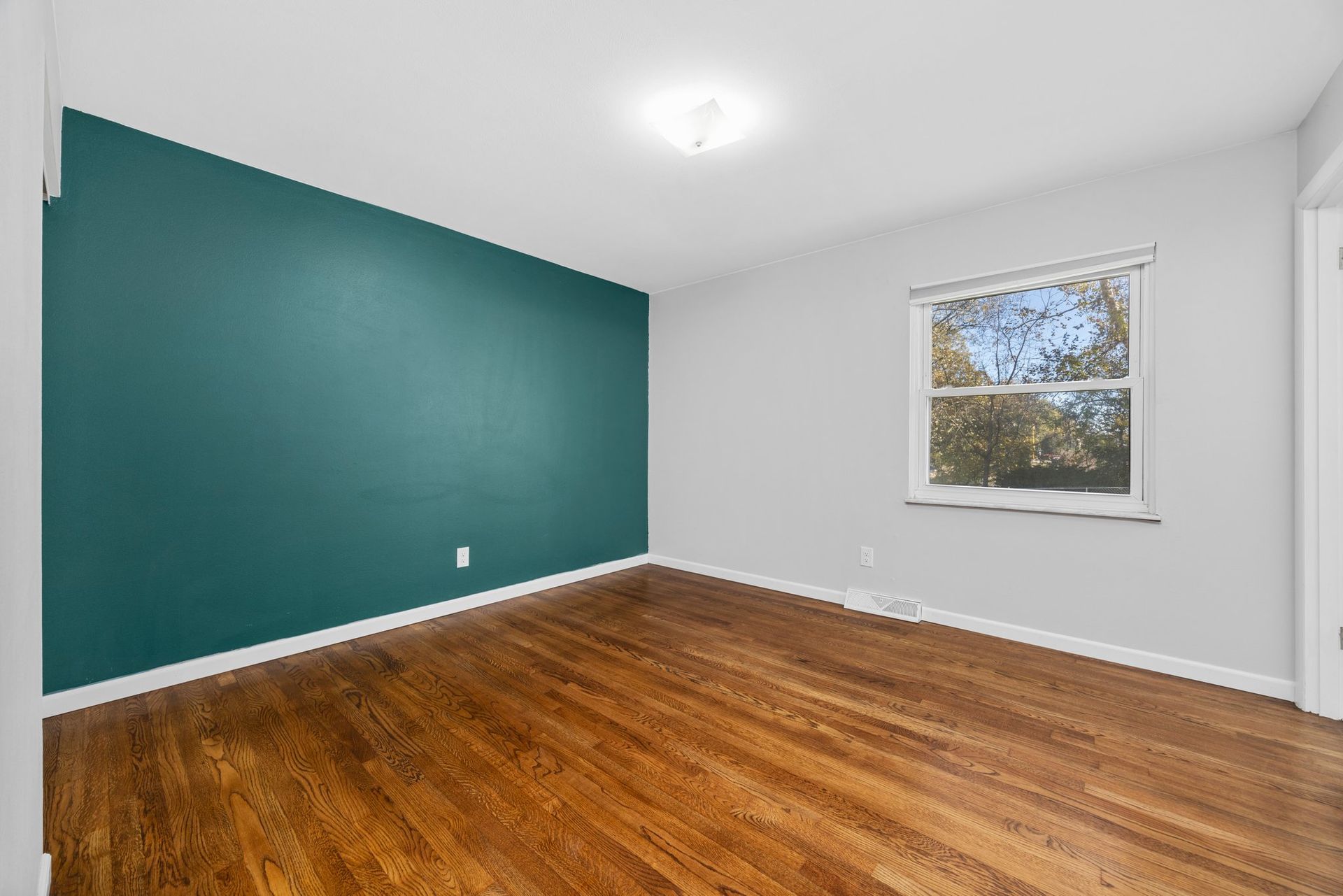 An empty room with hardwood floors and a window.