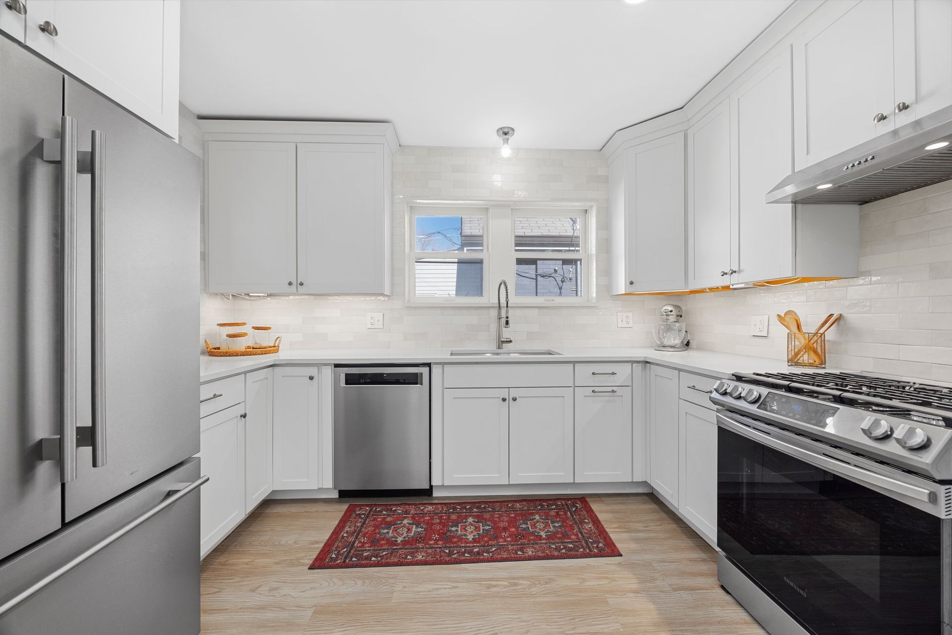 A kitchen with white cabinets , stainless steel appliances and a rug on the floor.