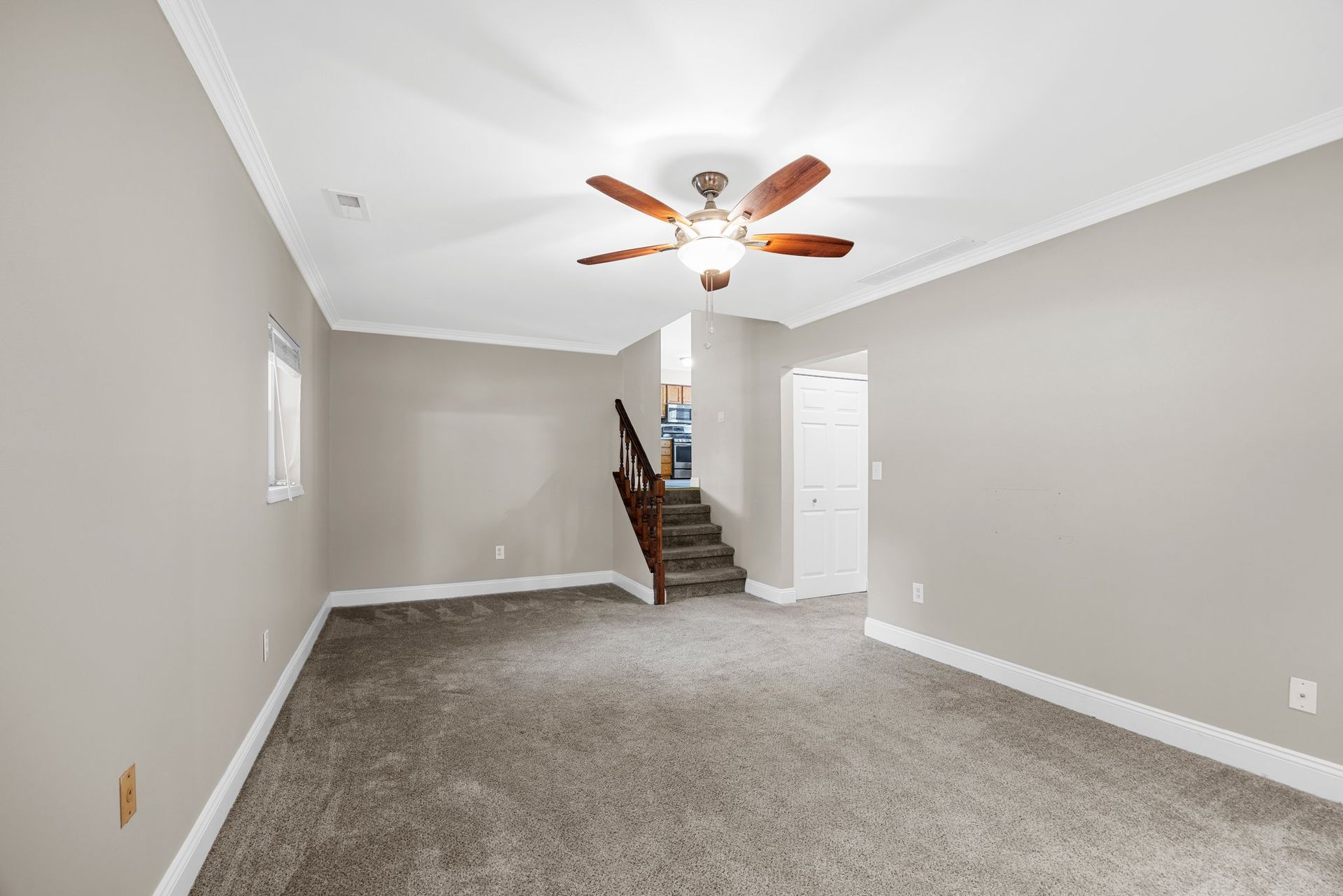 An empty basement with a ceiling fan and stairs.