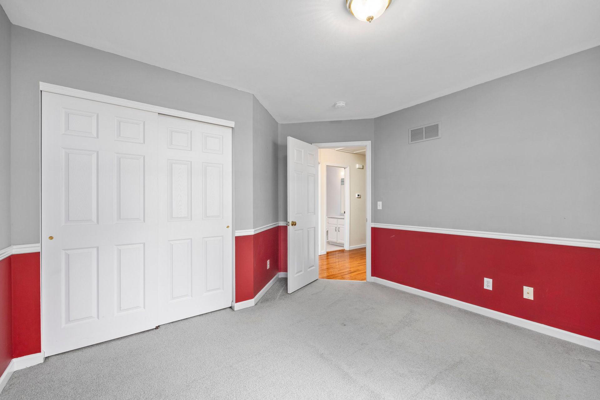 An empty bedroom with red and gray walls and a closet.