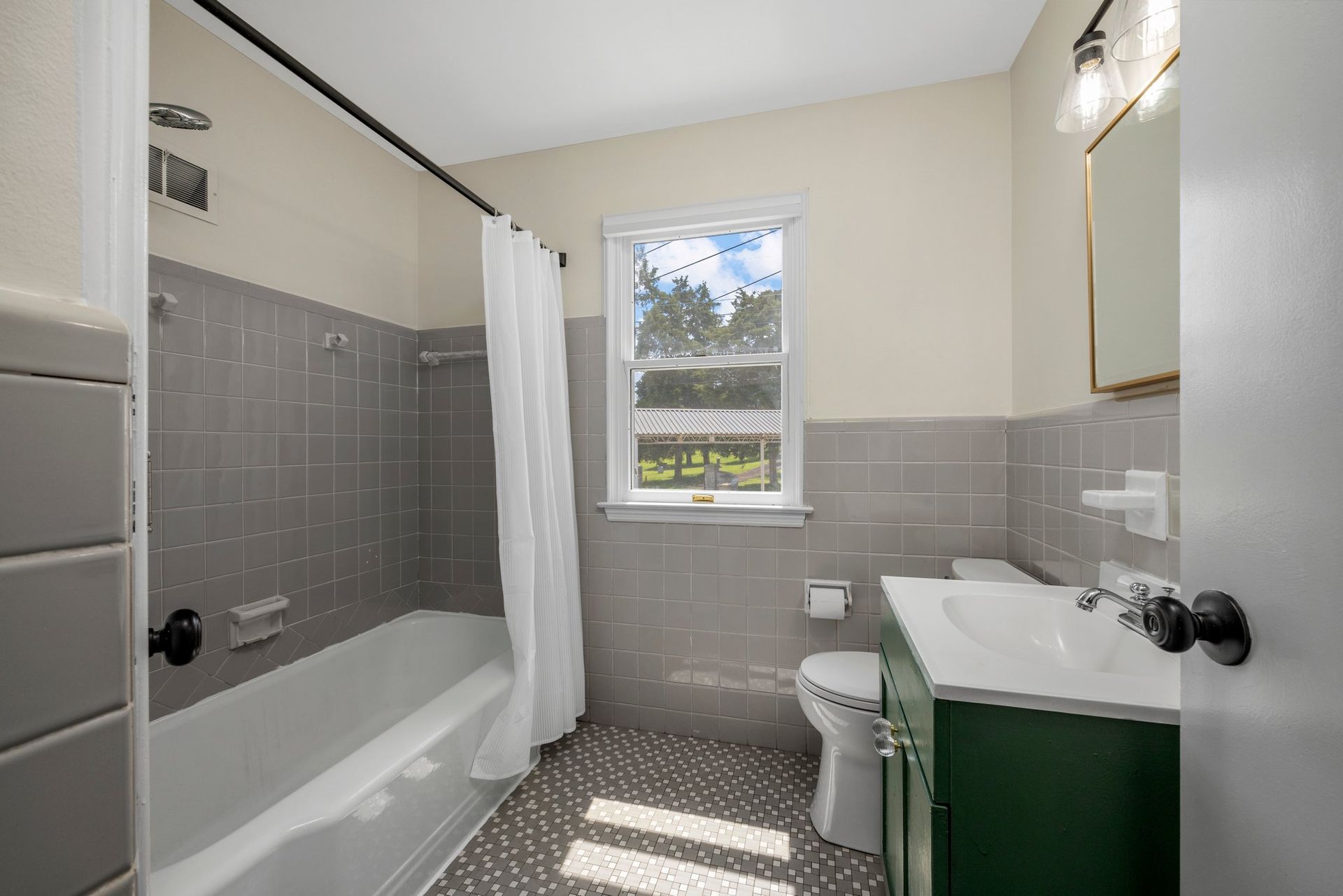 A bathroom with a tub , toilet , sink and window.