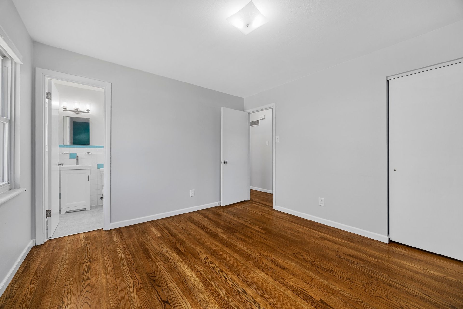 An empty bedroom with hardwood floors and white walls.