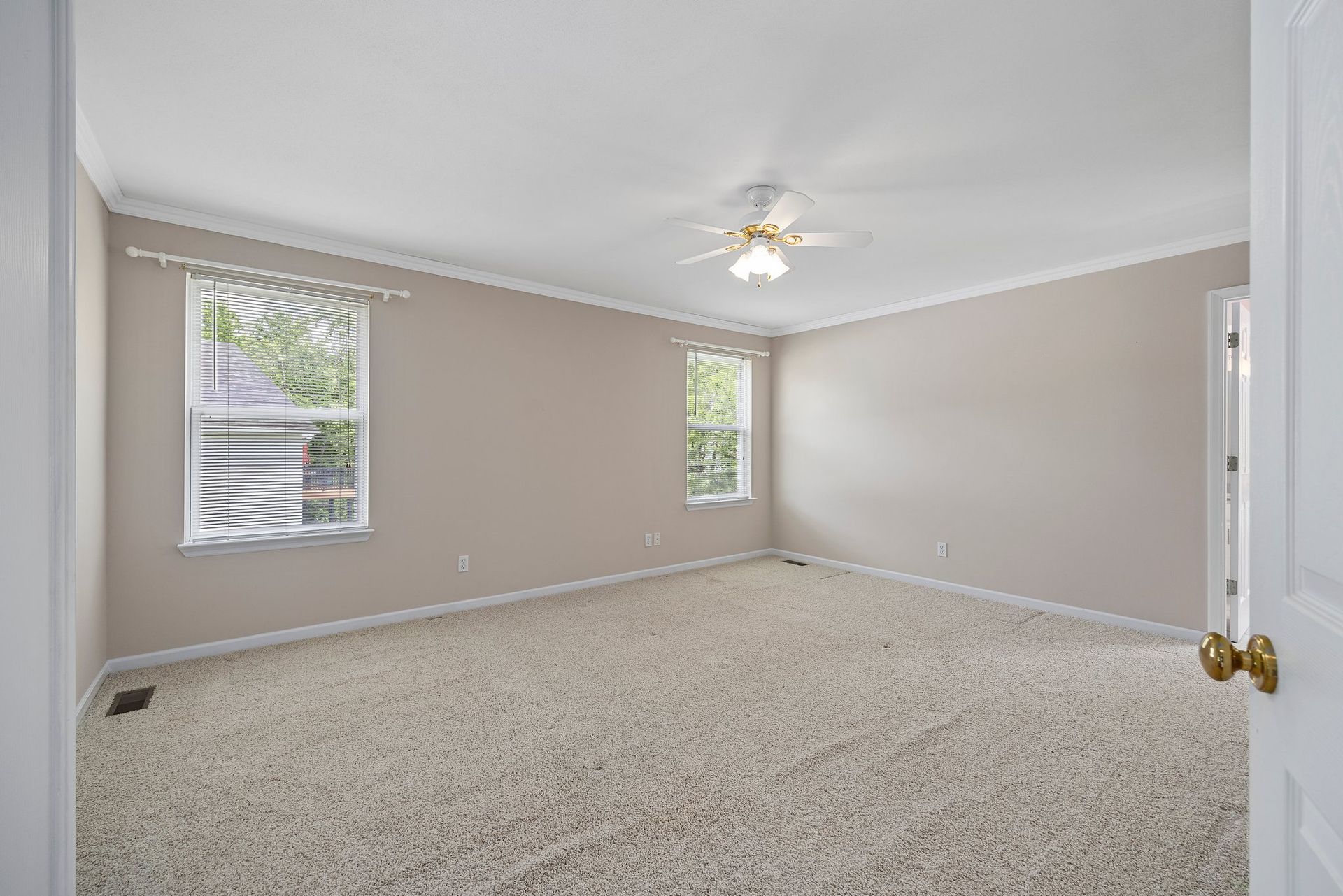 An empty bedroom with a ceiling fan and two windows.