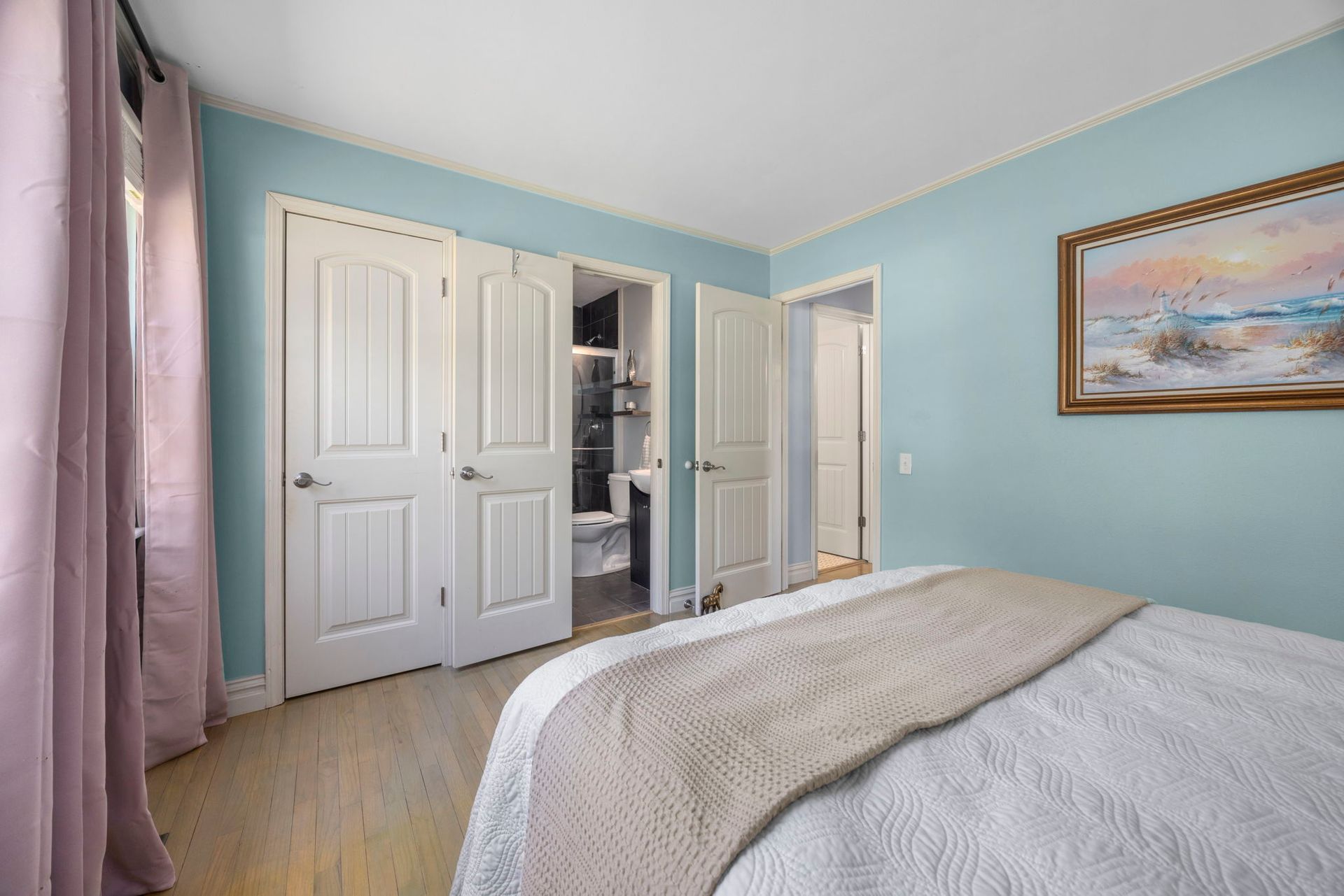Bedroom with light blue walls, white doors, a bed, and a framed painting.