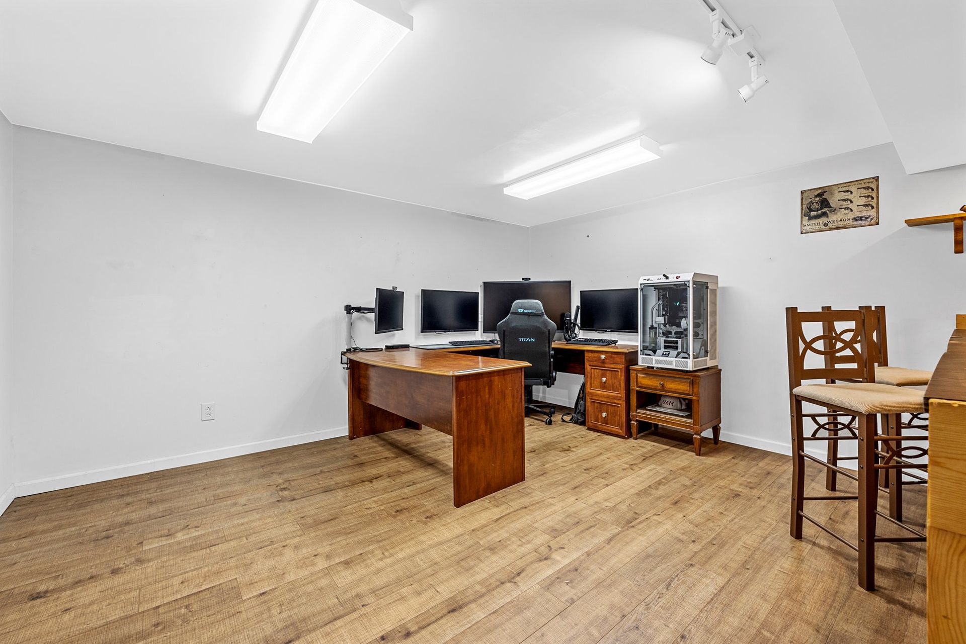 A room with a wooden floor , a desk , chairs and computers.