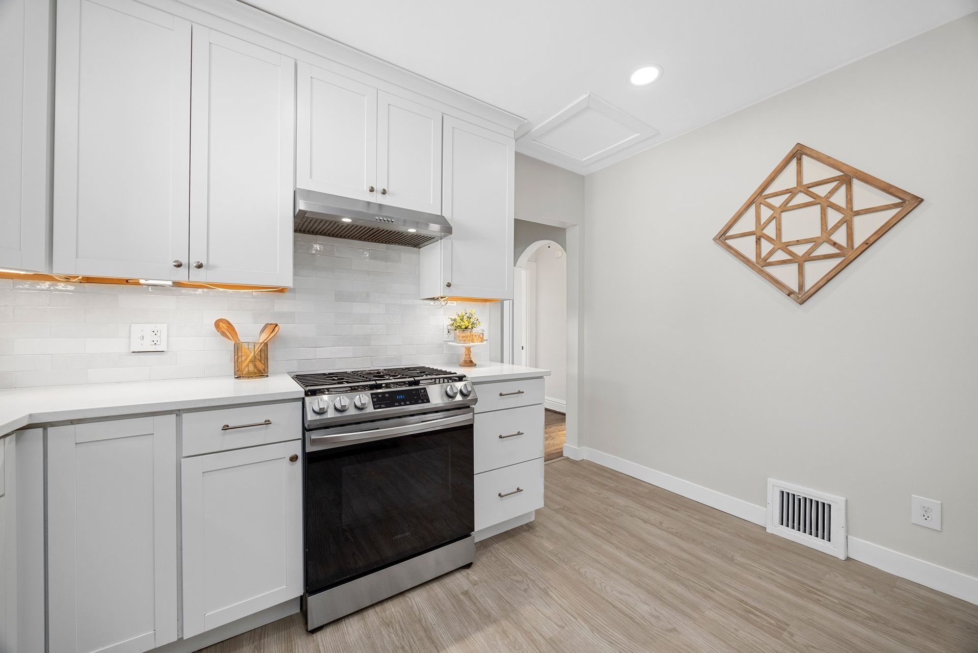 A kitchen with white cabinets , a stove , and a wooden floor.