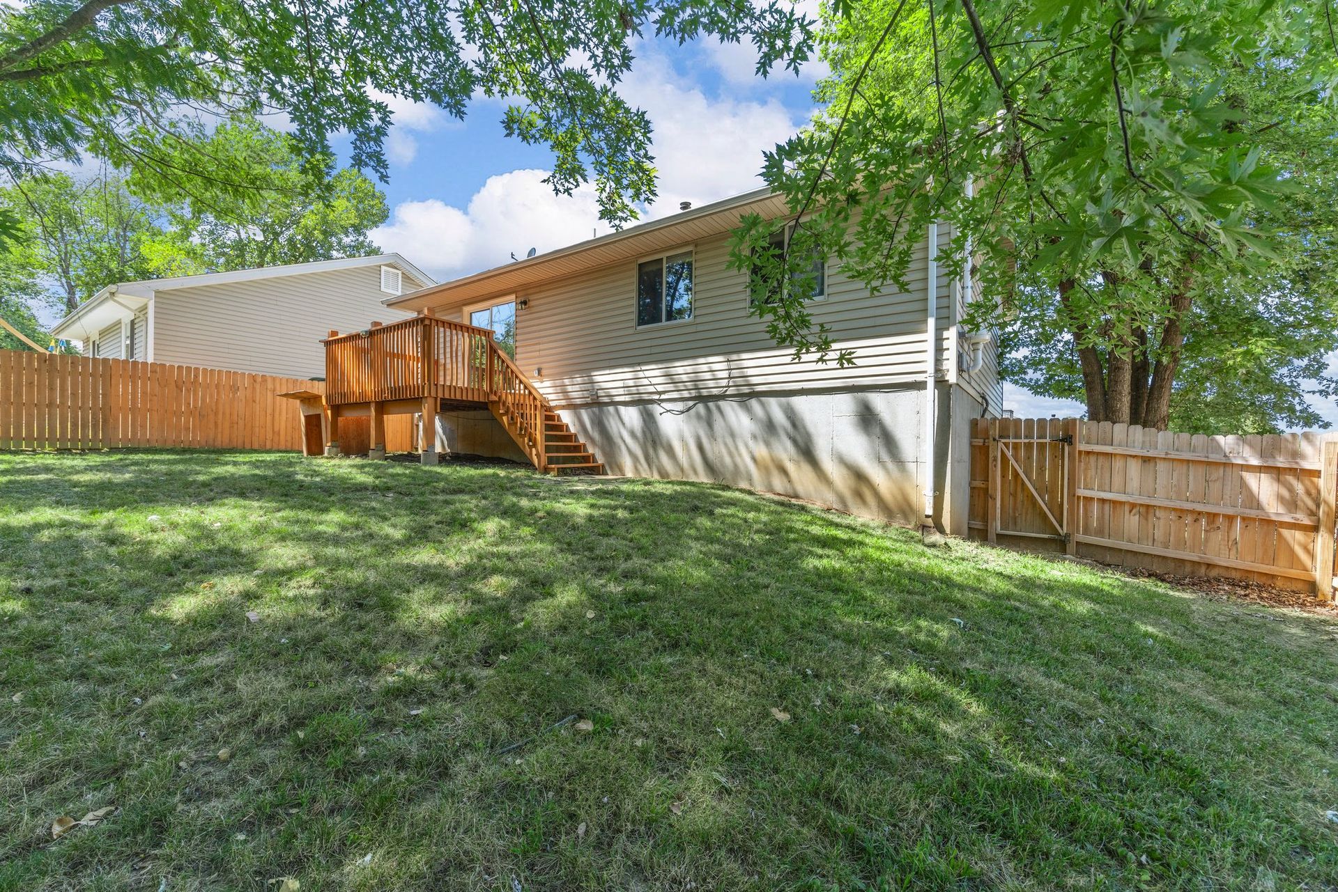 The backyard of a house with a large lawn and a wooden deck.