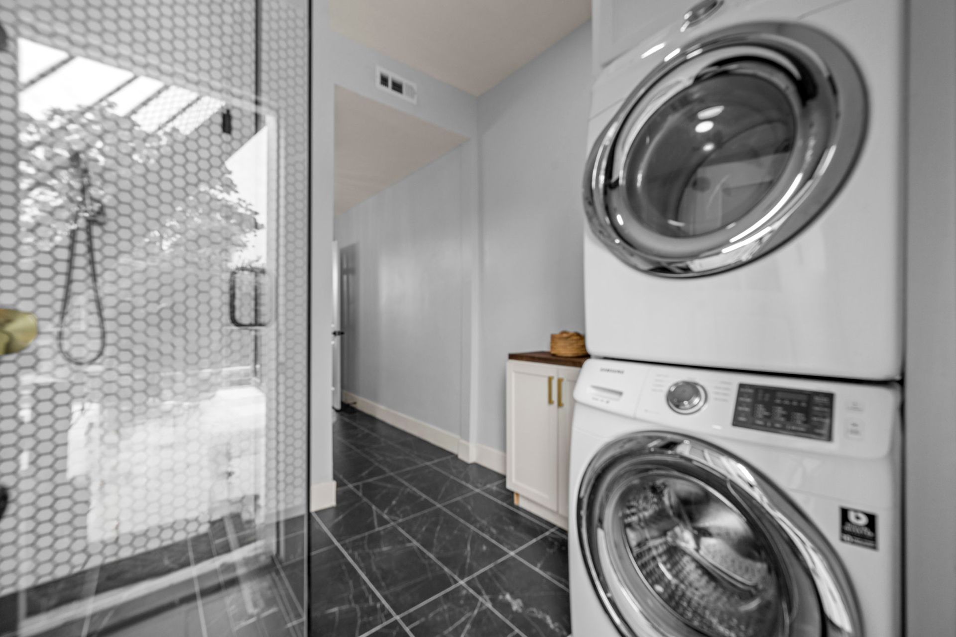 Laundry room with stacked white washer/dryer, black tiled floor, and walk-in shower.