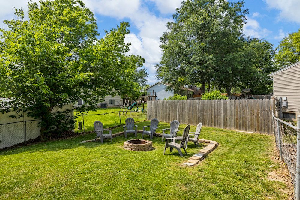 A backyard with a fire pit and chairs in the grass.