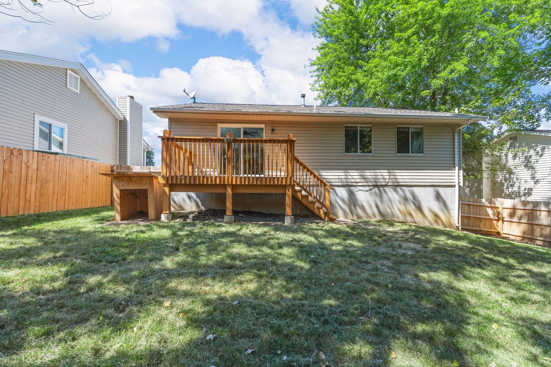 The backyard of a house with a large deck and a wooden fence.