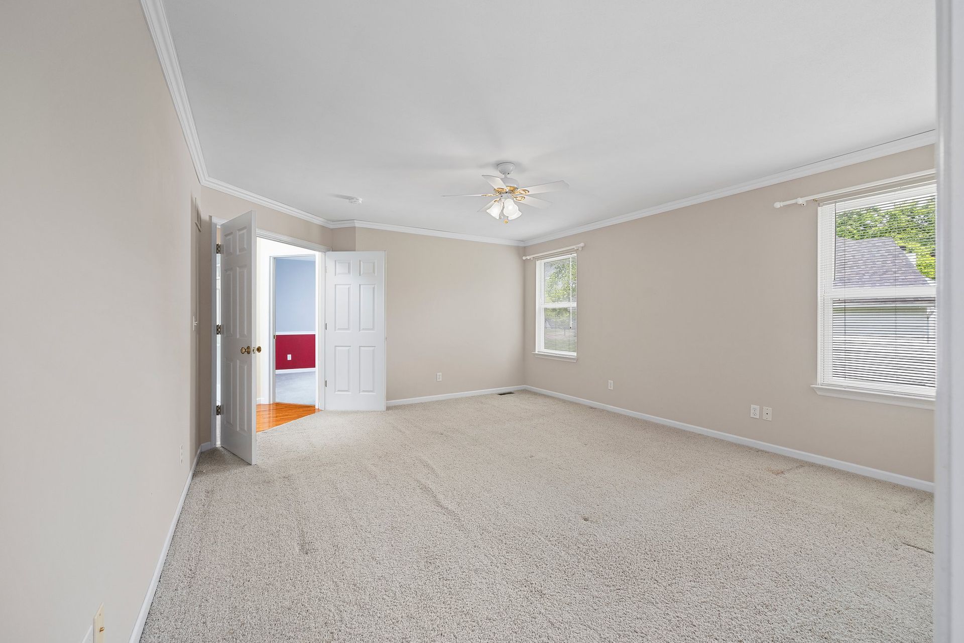 An empty bedroom with a ceiling fan and two windows.