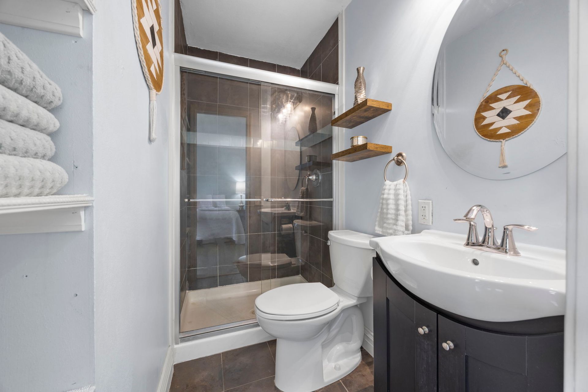 Bathroom with shower, toilet, sink, and decorative shelves. Blue walls and dark wood floors.