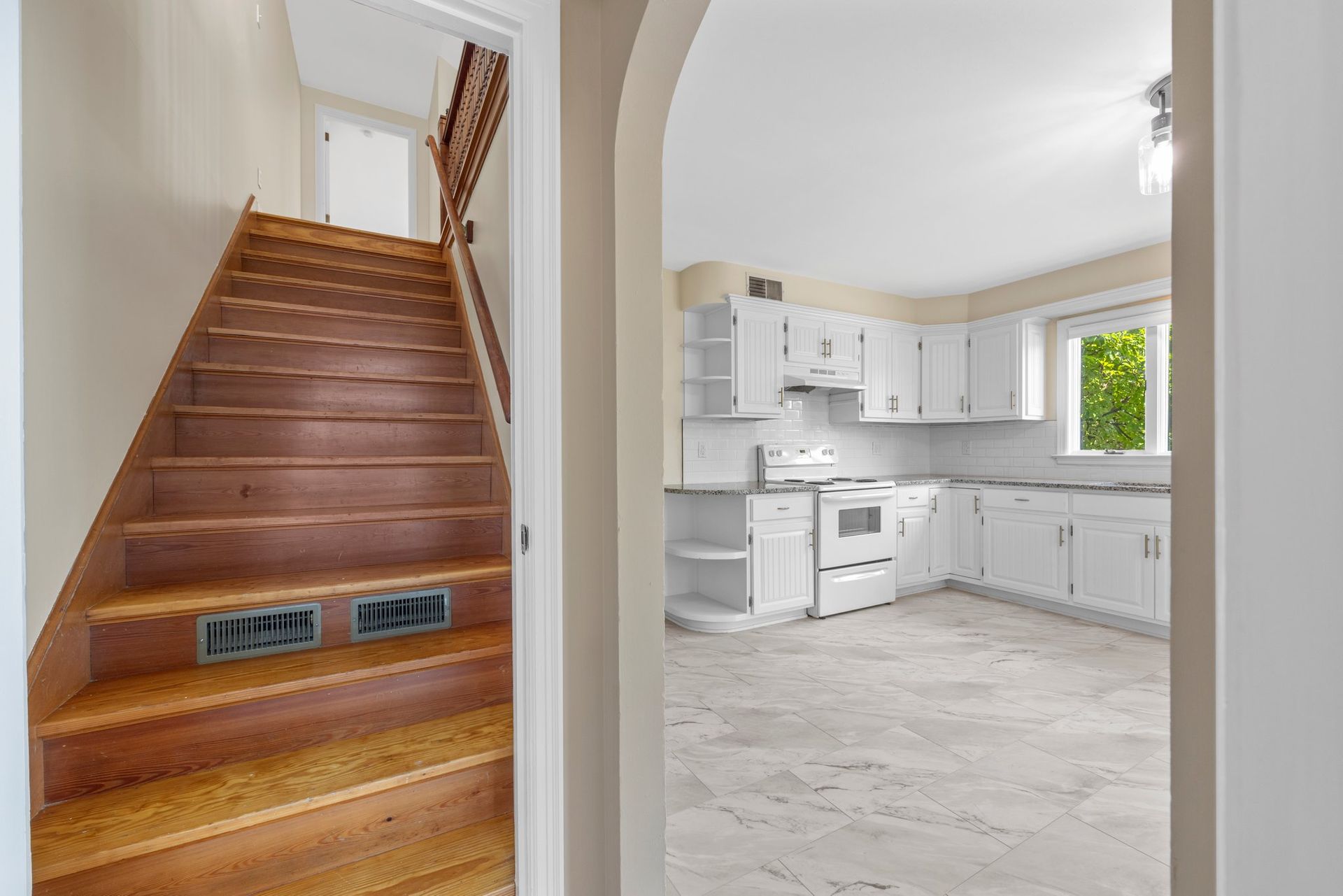 A kitchen with white cabinets and a wooden staircase leading up to it.