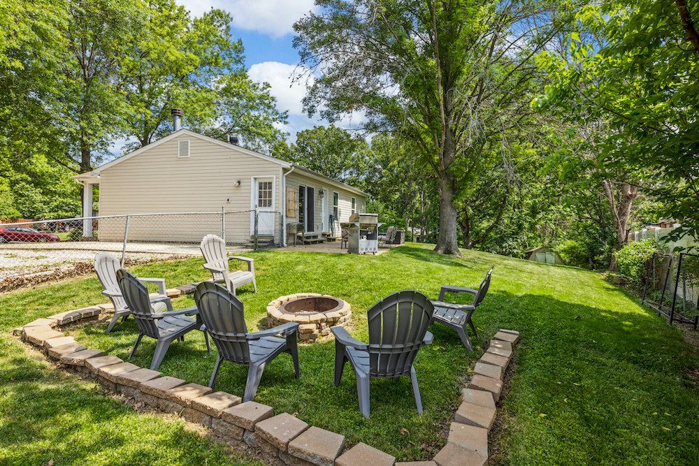 There is a fire pit in the middle of the yard with chairs around it.
