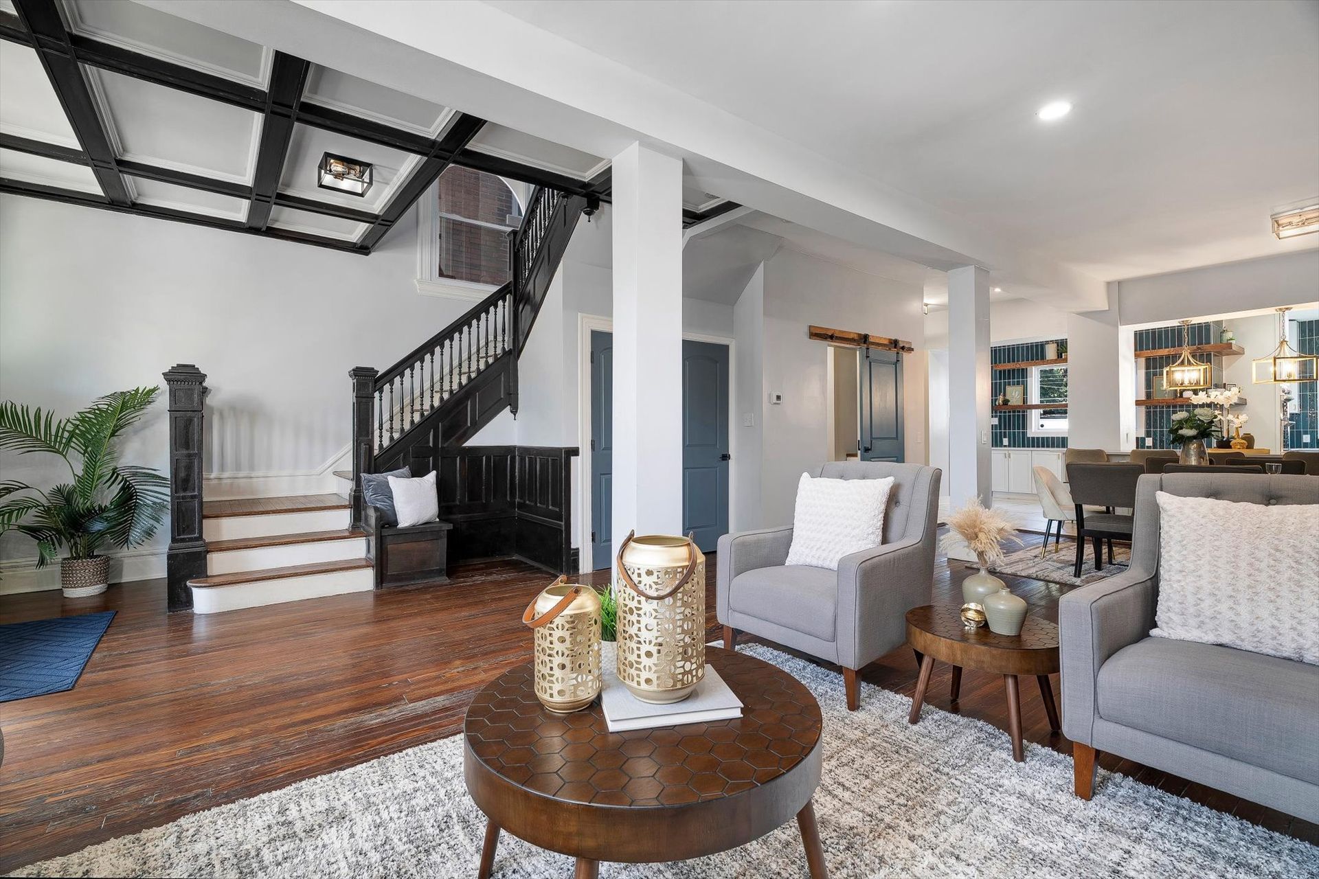 Living room with staircase, gray armchairs, and a coffee table with gold lanterns.