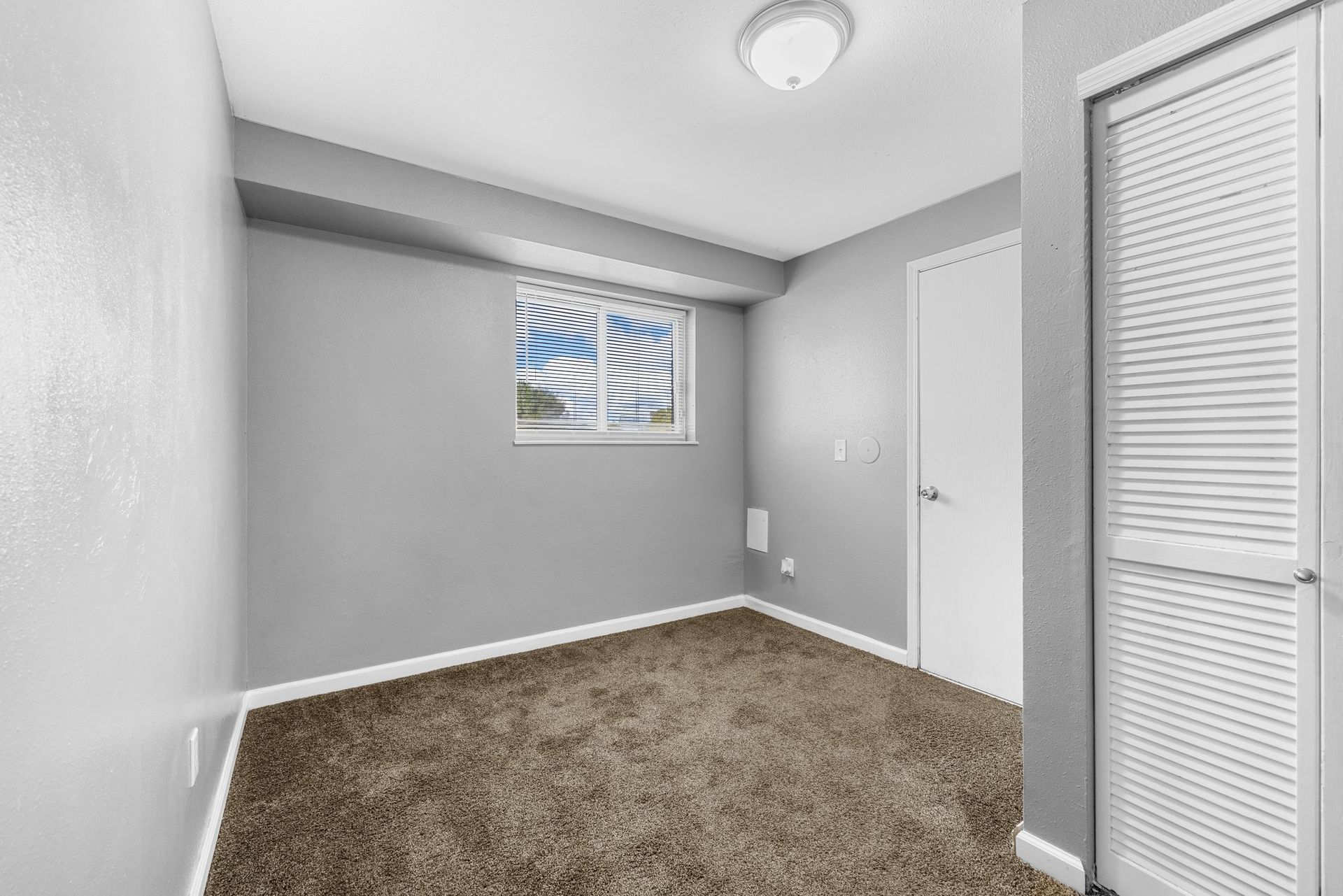 An empty bedroom with a window and a closet.