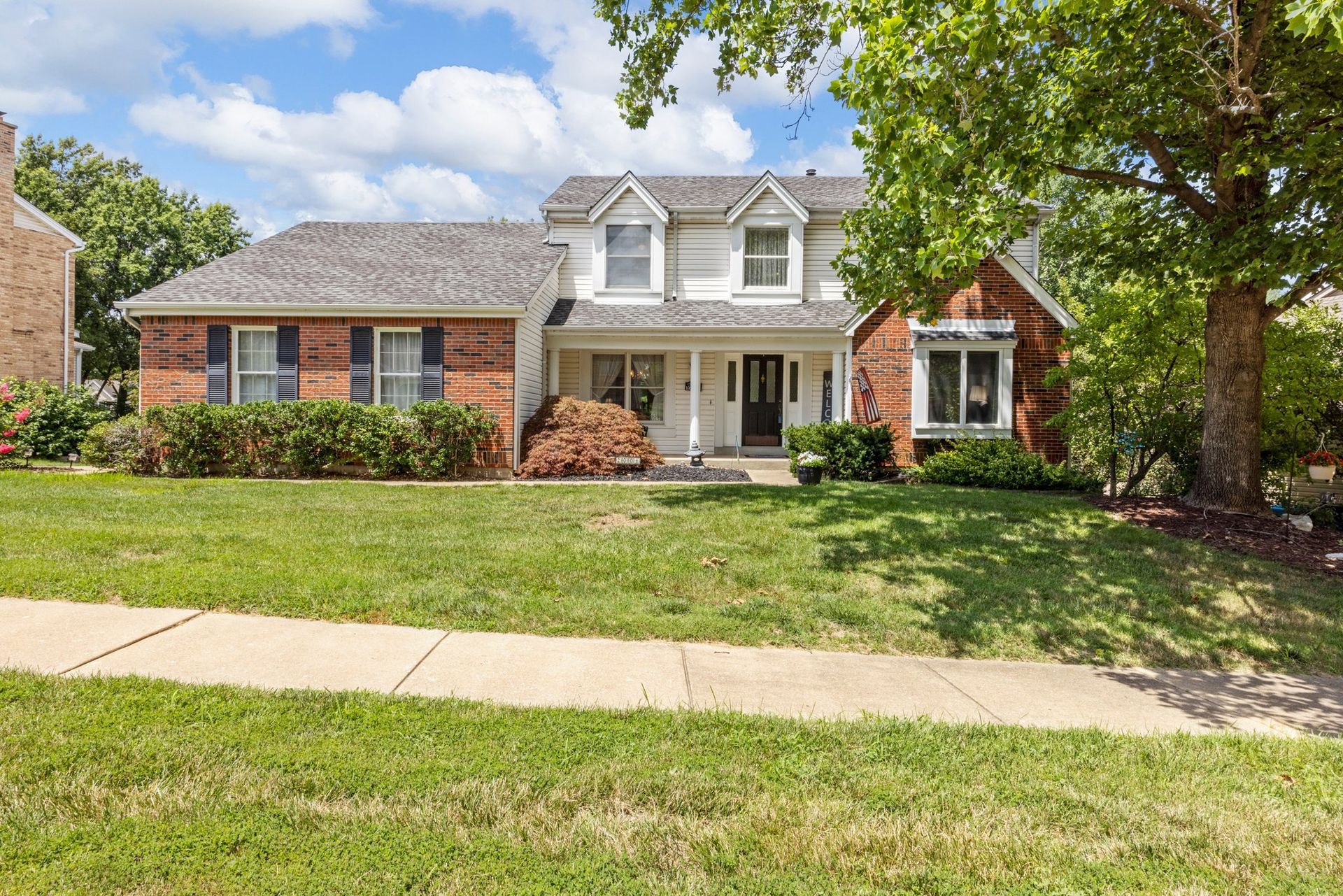 A large brick house with a large lawn and a tree in front of it.