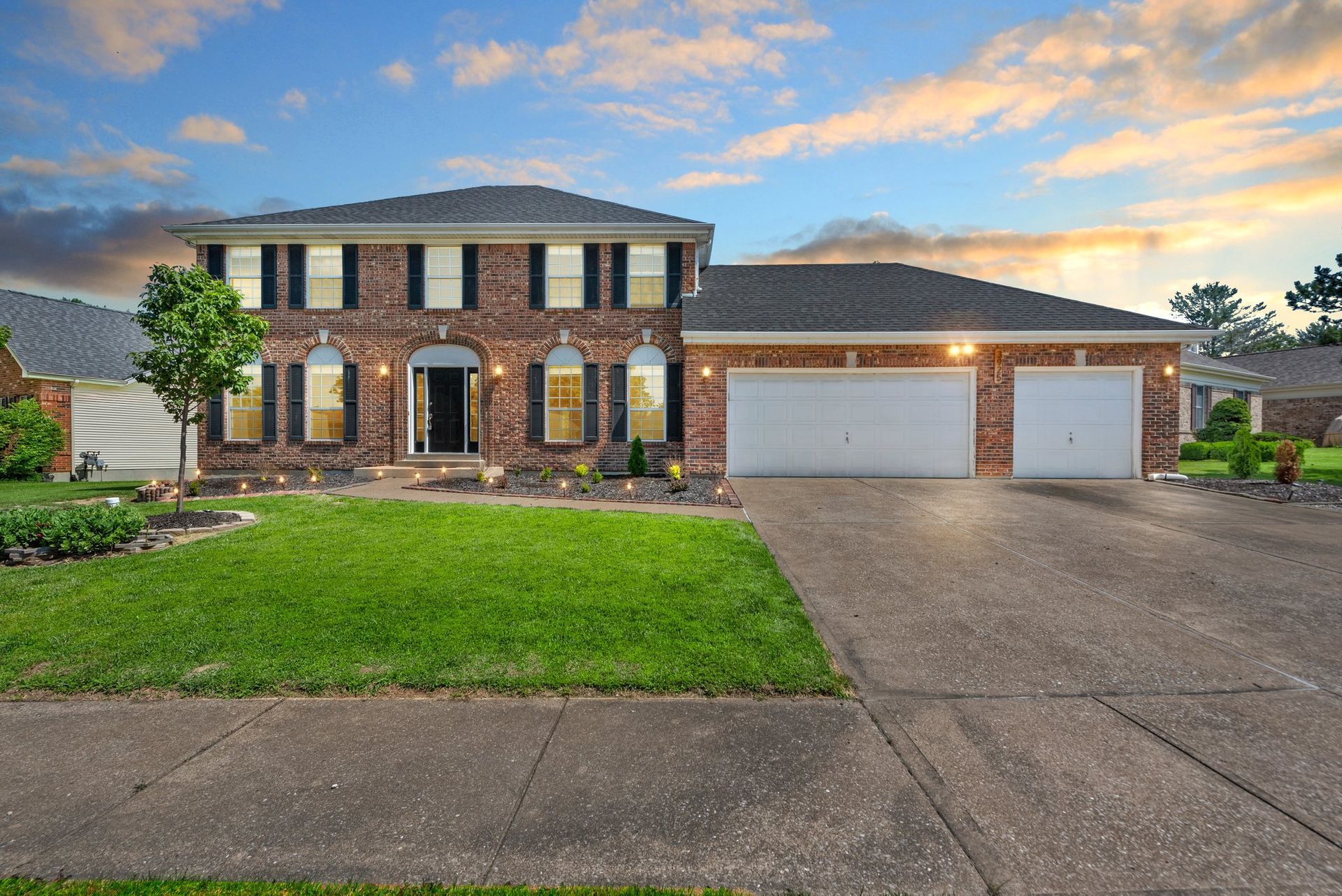 A large brick house with two garages and a lush green lawn