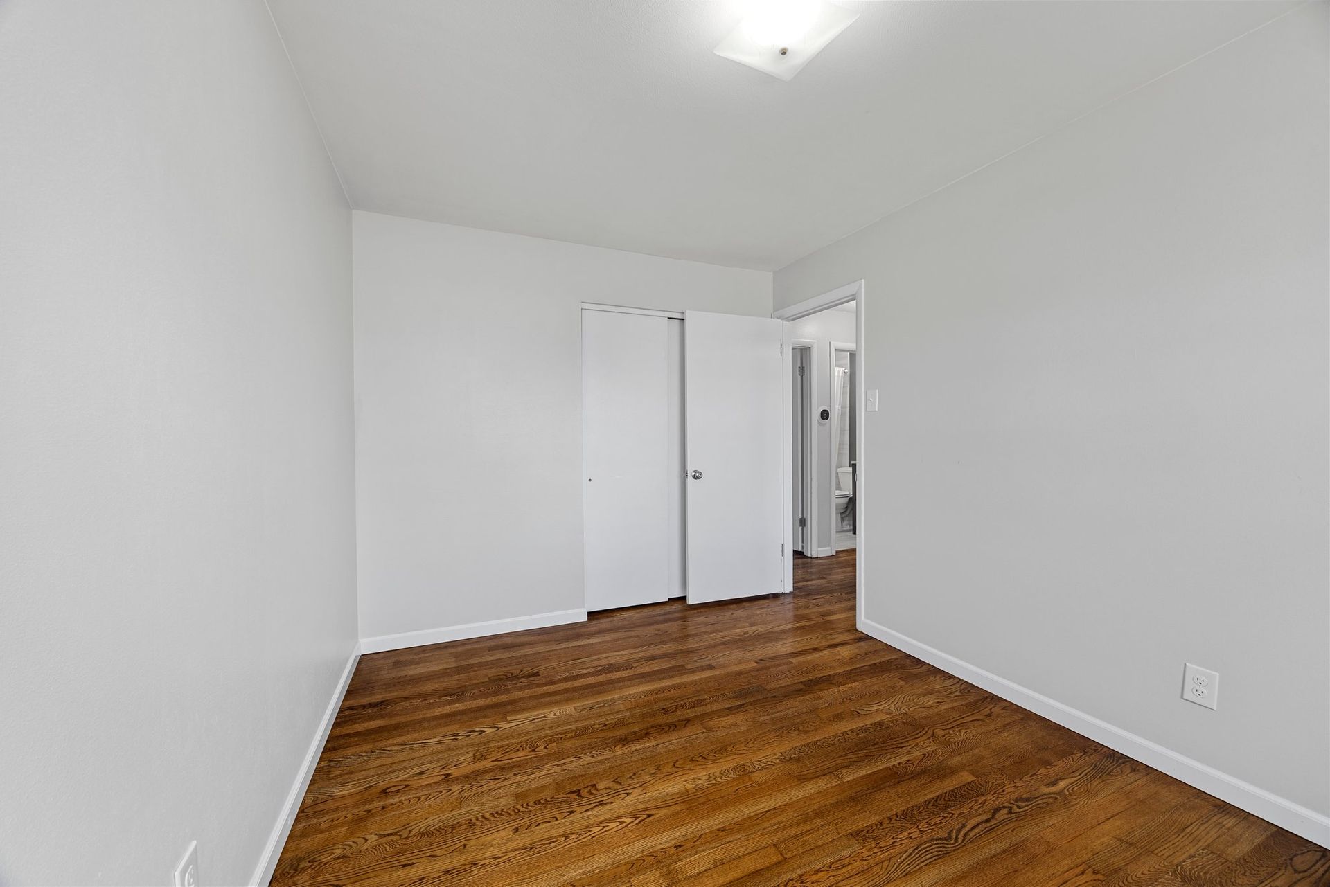 An empty bedroom with hardwood floors and white walls.