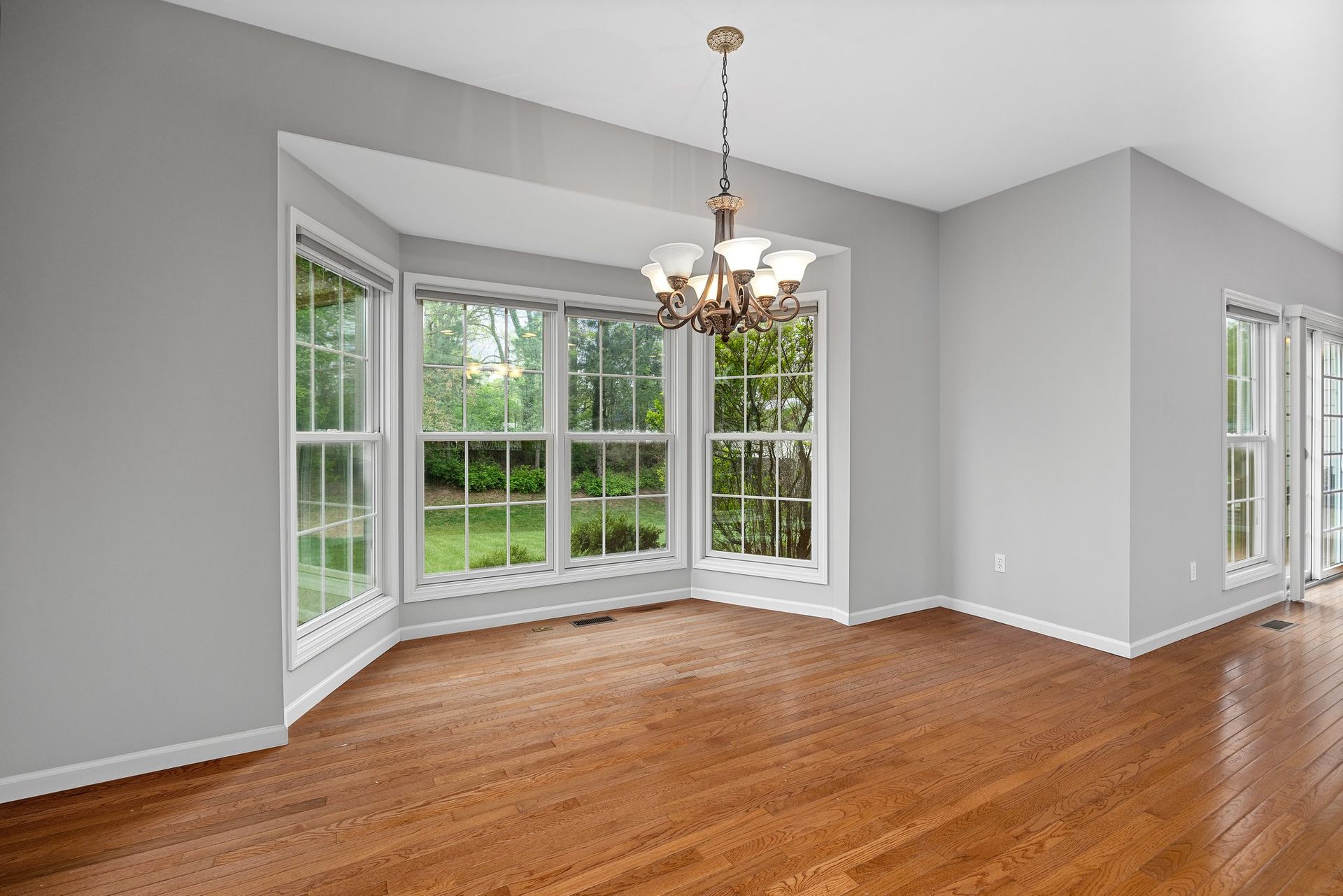 An empty dining room with hardwood floors and a chandelier.