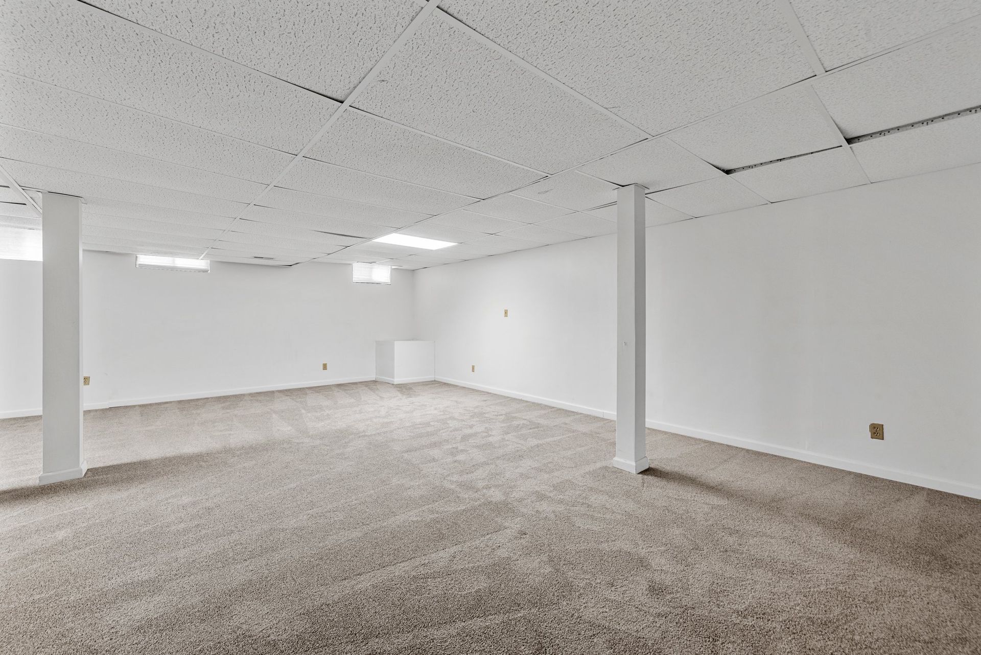 An empty basement with a carpeted floor and white walls.