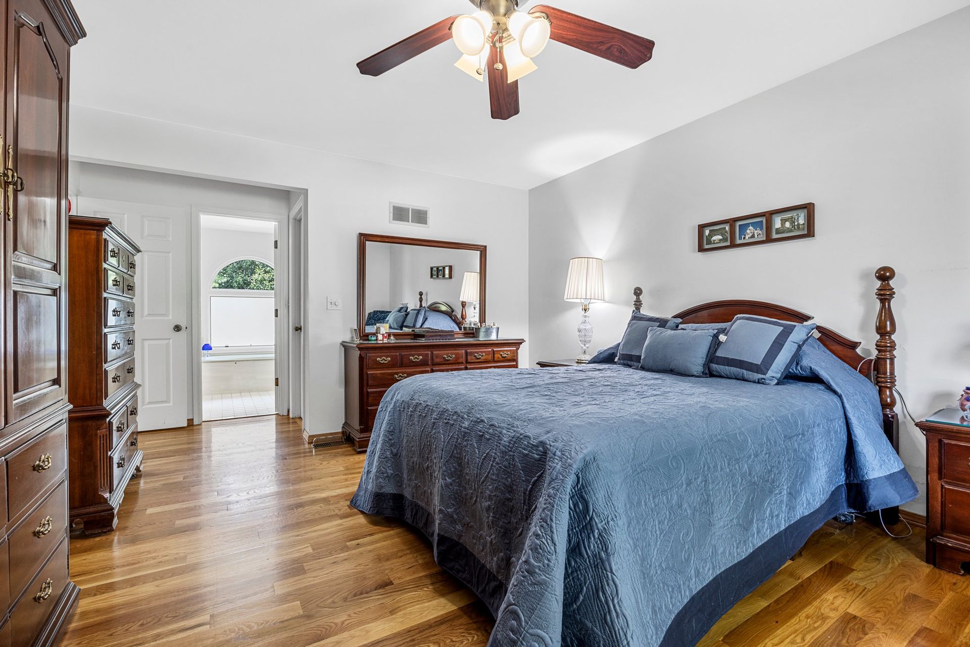 A bedroom with a bed , dresser , mirror and ceiling fan.