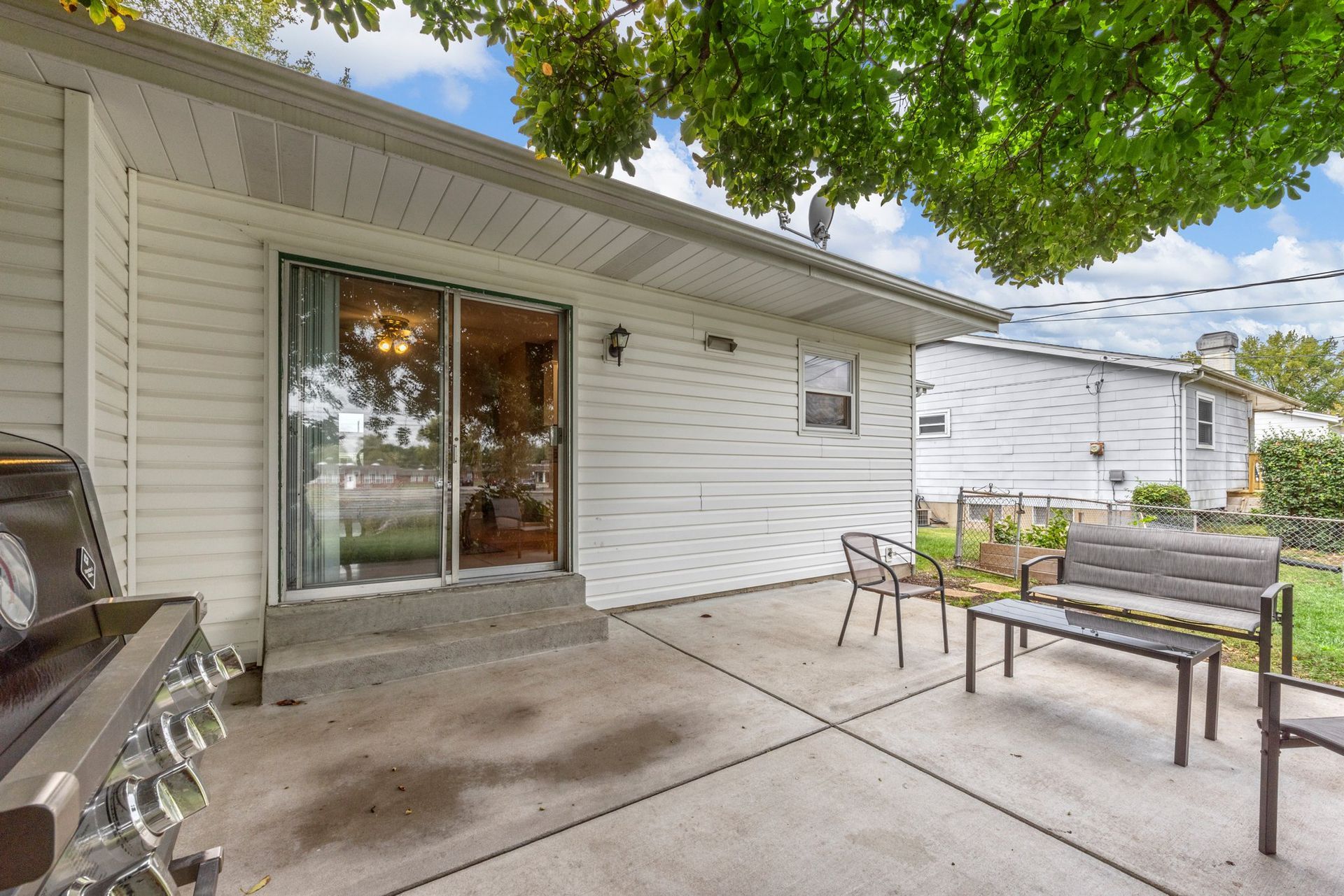 A patio with a grill and a bench in front of a house.