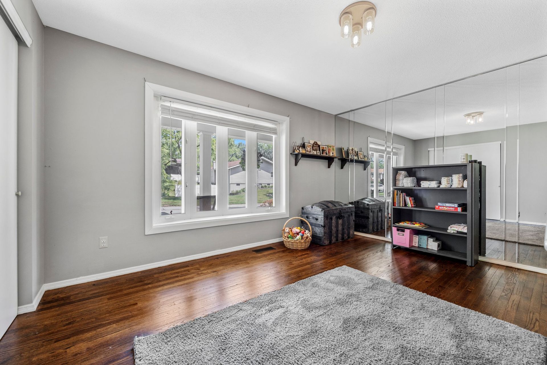 A living room with hardwood floors , a rug , a bookshelf and a large mirror.