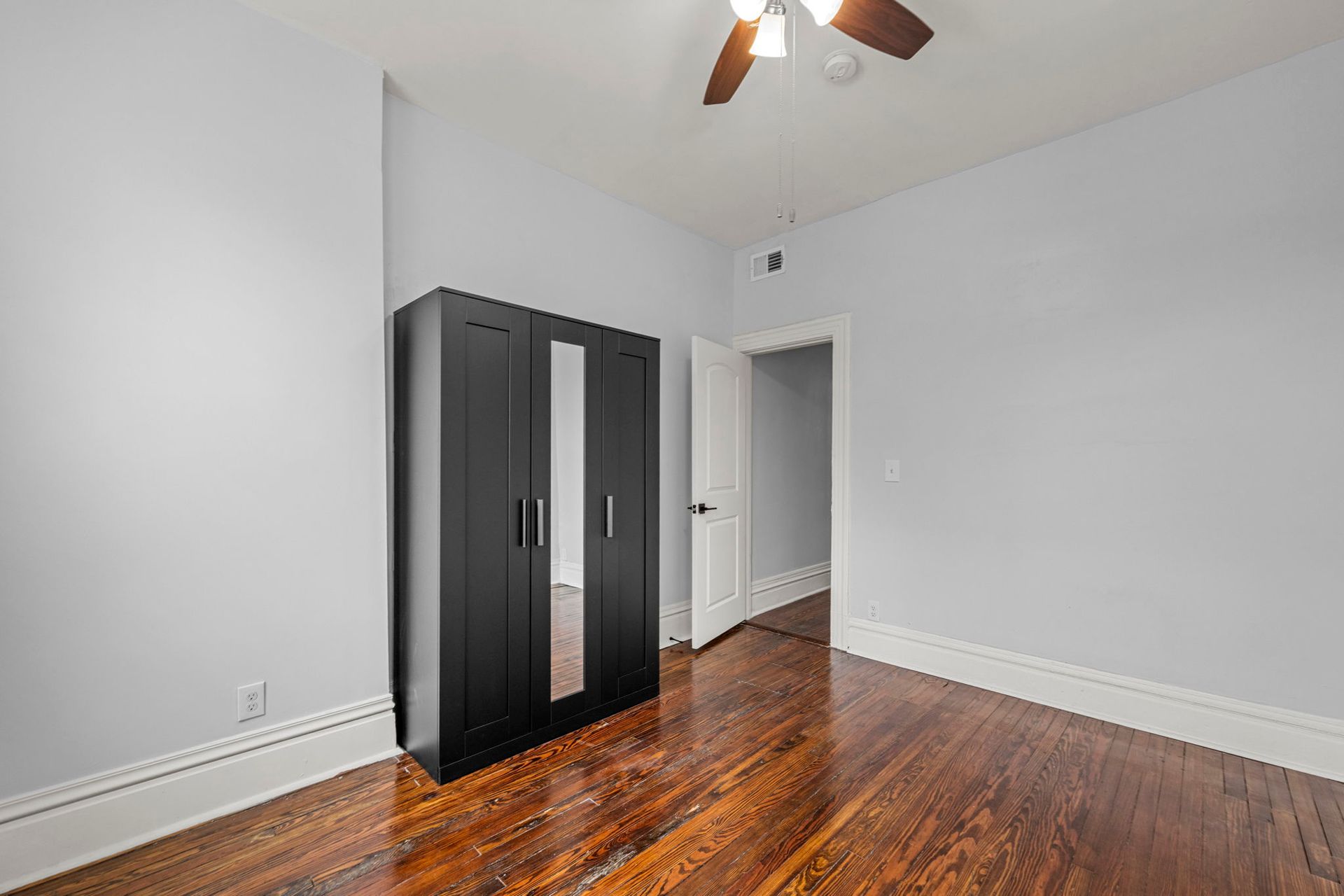 Bedroom with dark wood floors, gray walls, black wardrobe, and open doorway.