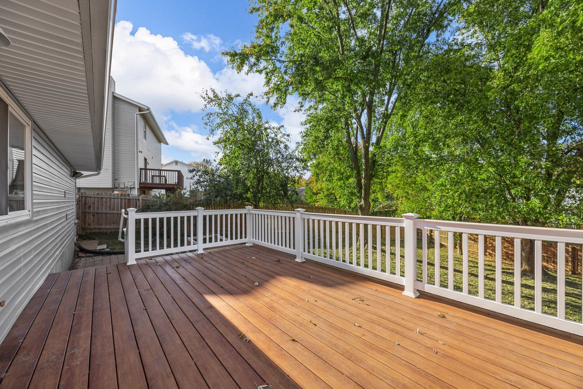 A large wooden deck with a white railing and trees in the background.