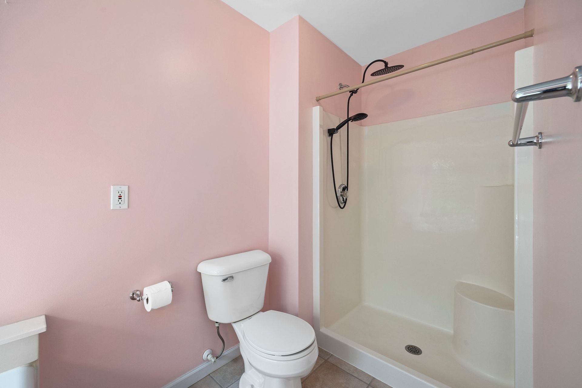A bathroom with a toilet , sink , shower and pink walls.