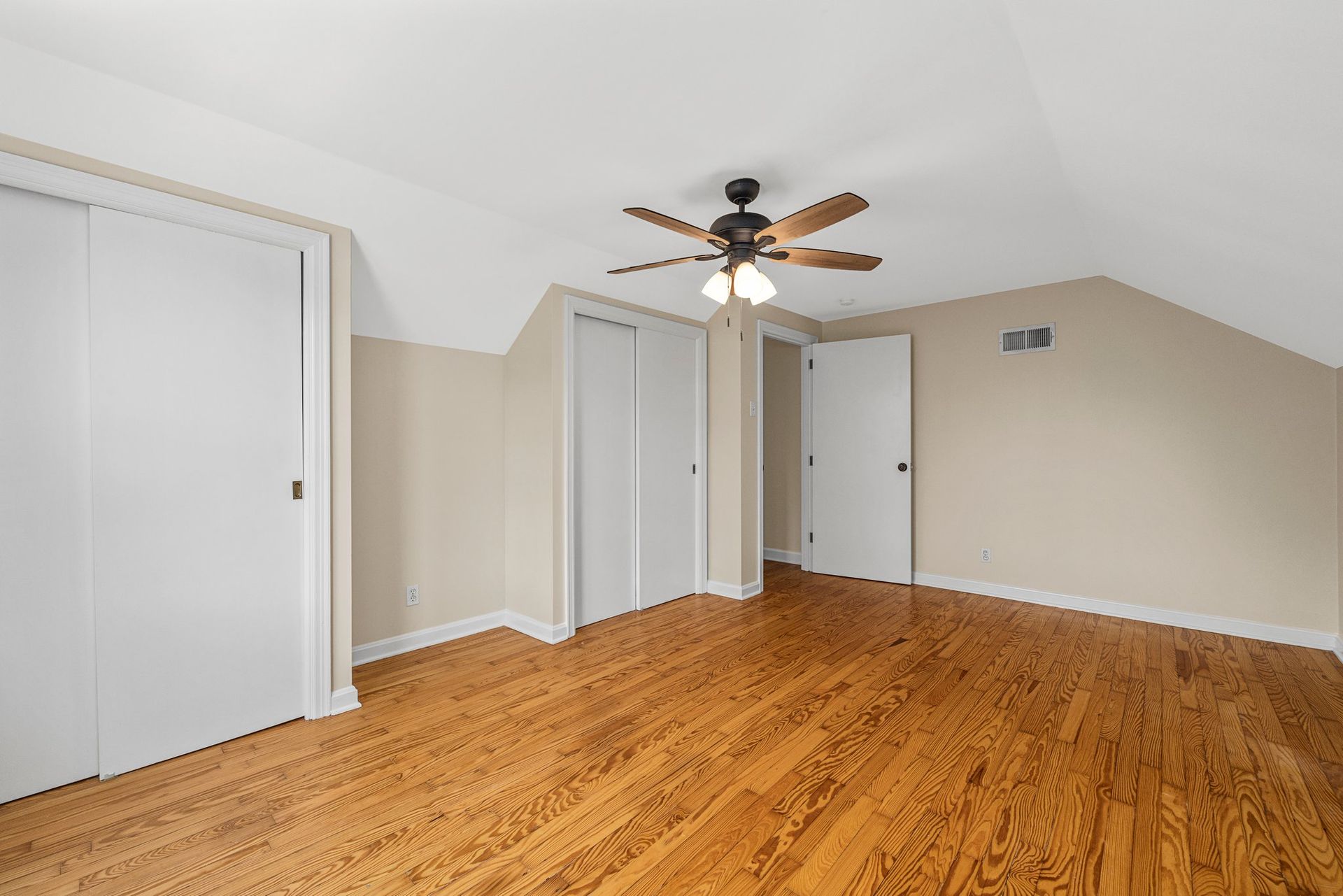 An empty bedroom with hardwood floors and a ceiling fan.