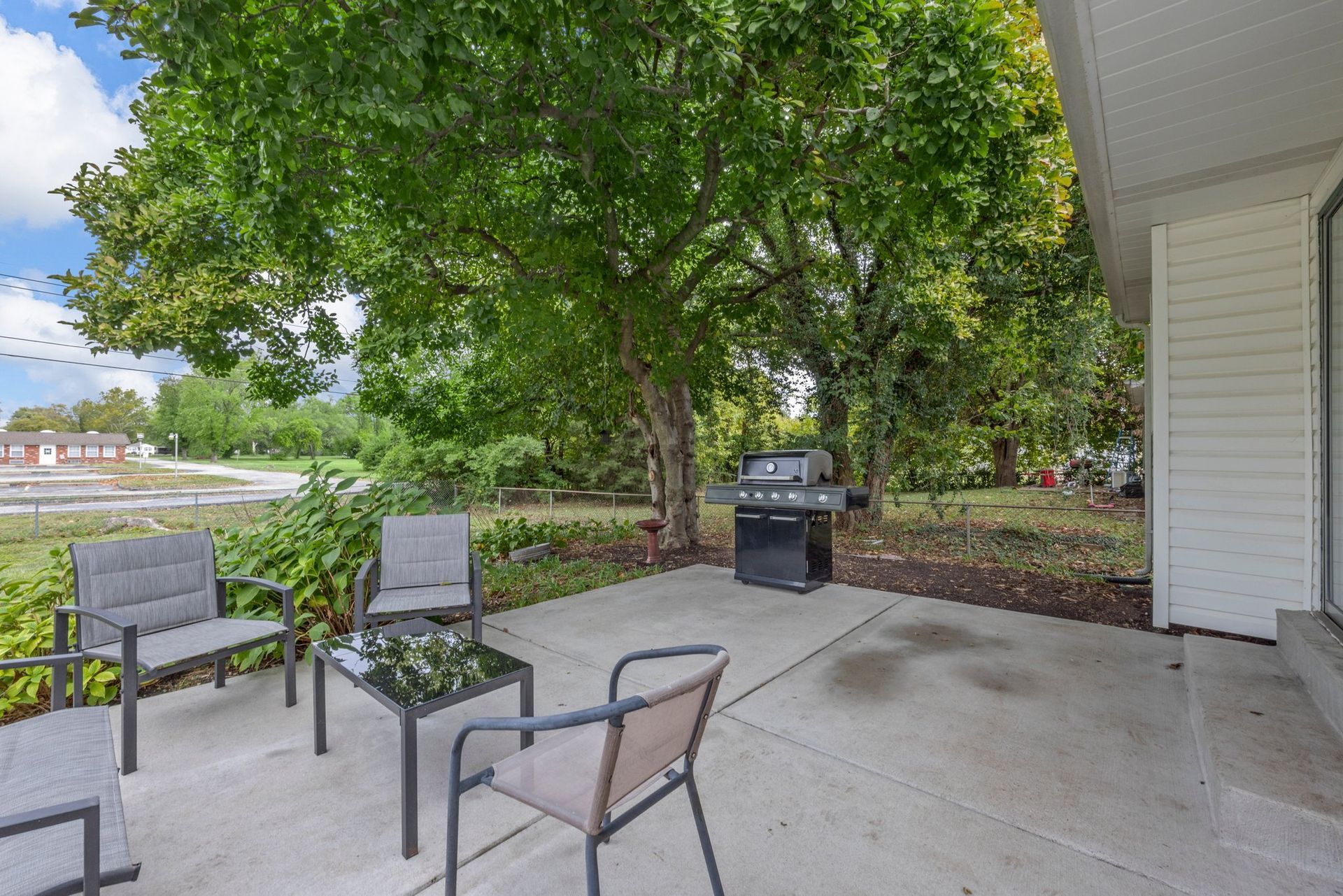 A patio with chairs , a table and a grill.