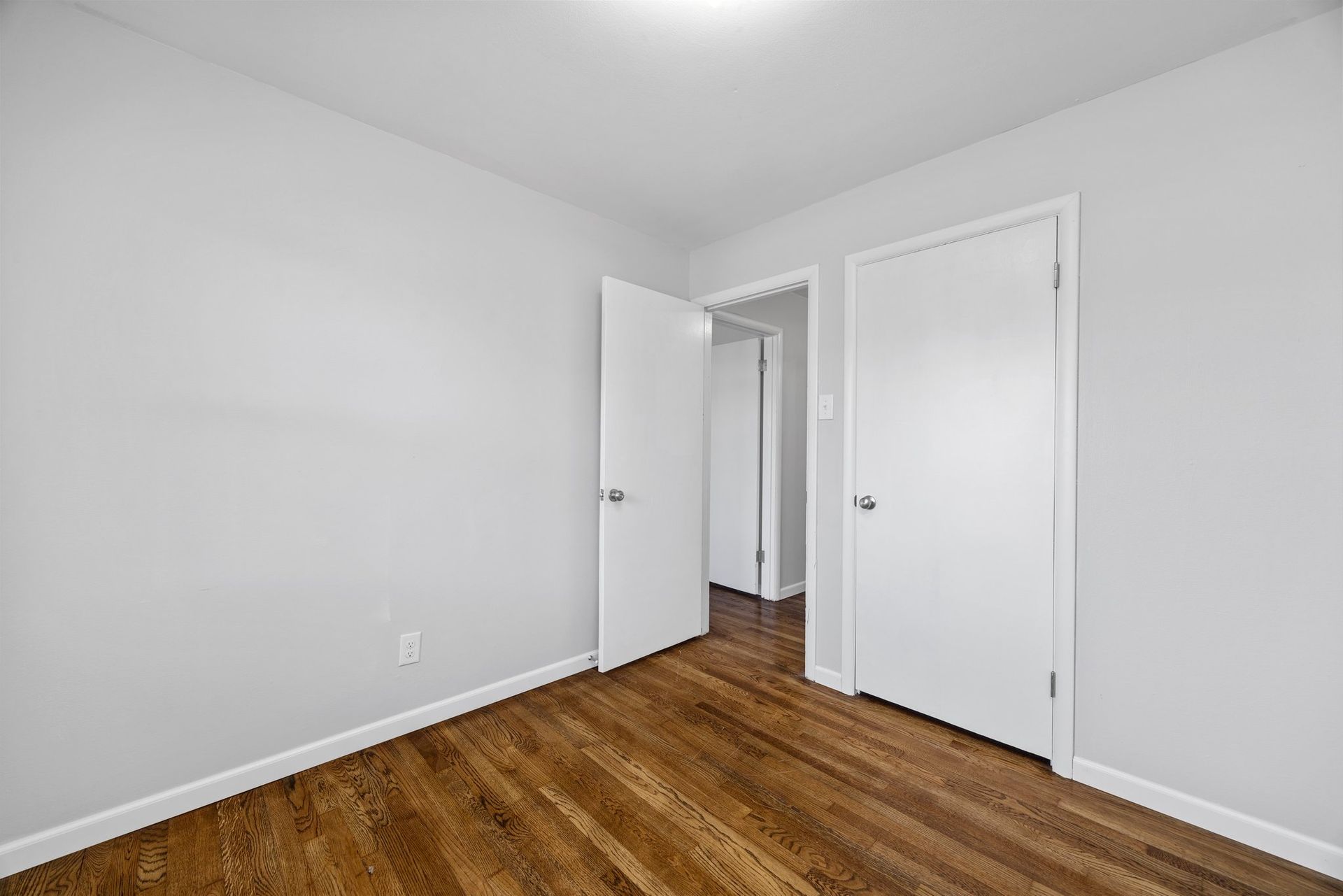 An empty bedroom with hardwood floors and white walls.