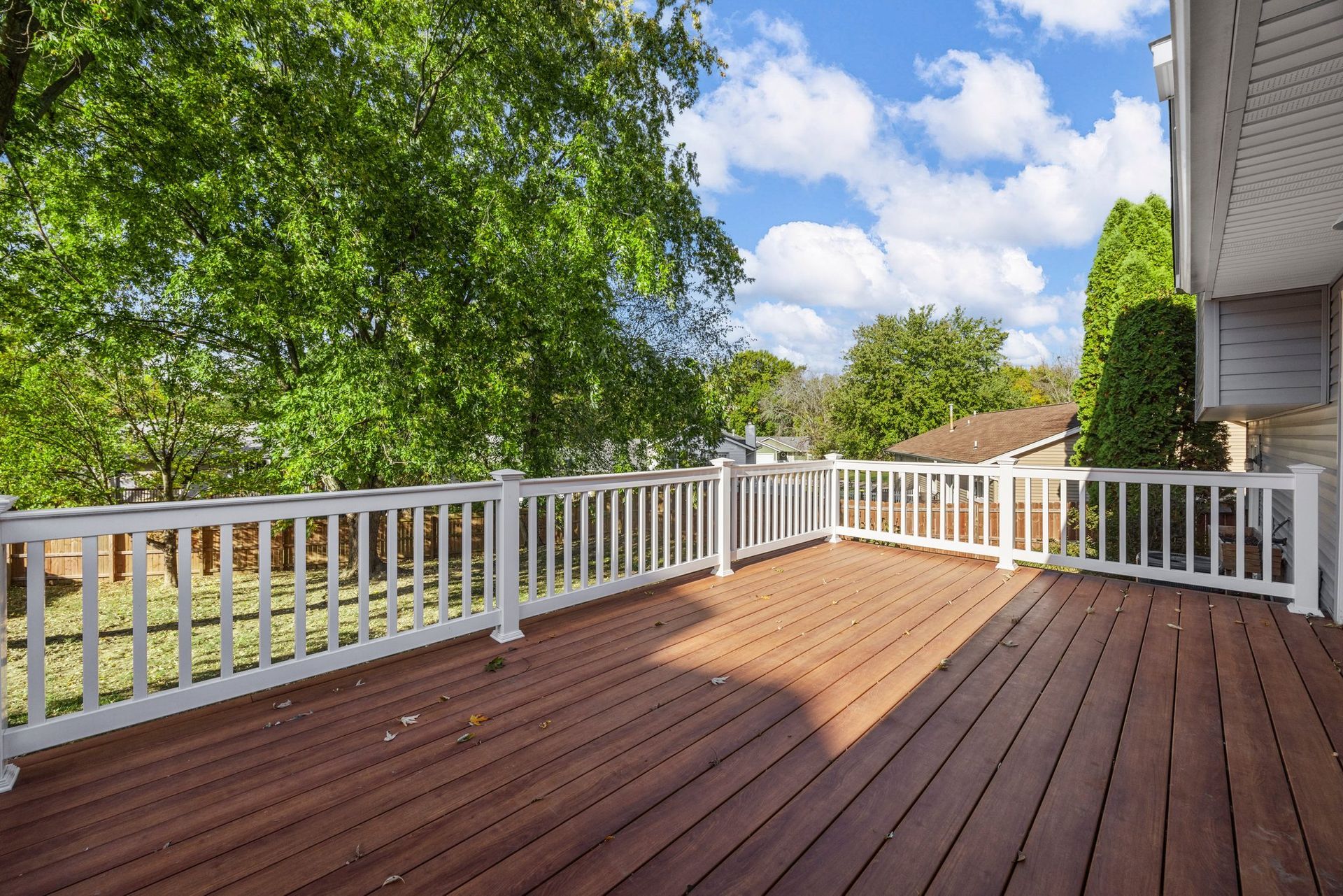 A large wooden deck with a white railing and trees in the background.