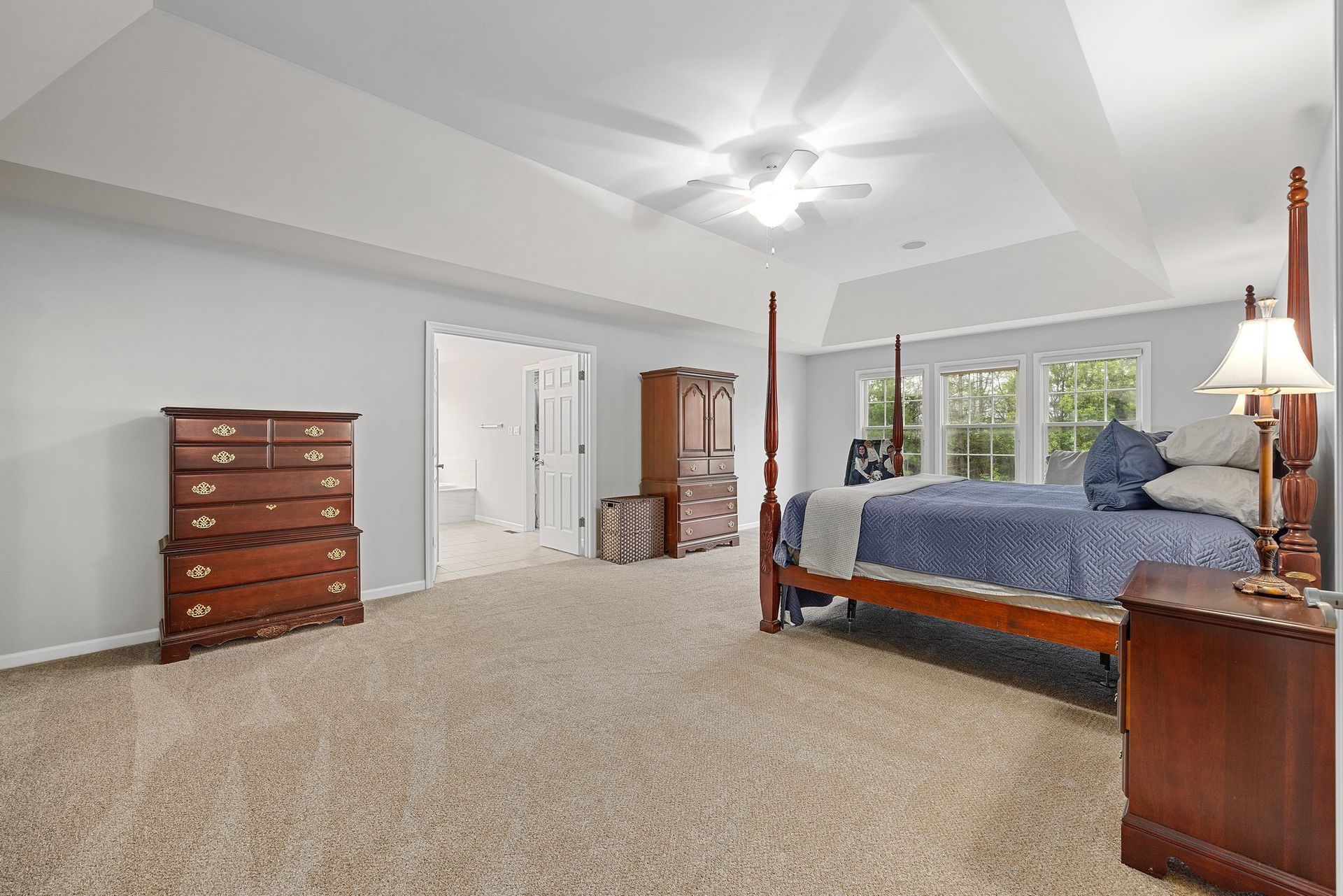 A bedroom with a four poster bed , dresser , nightstand and ceiling fan.
